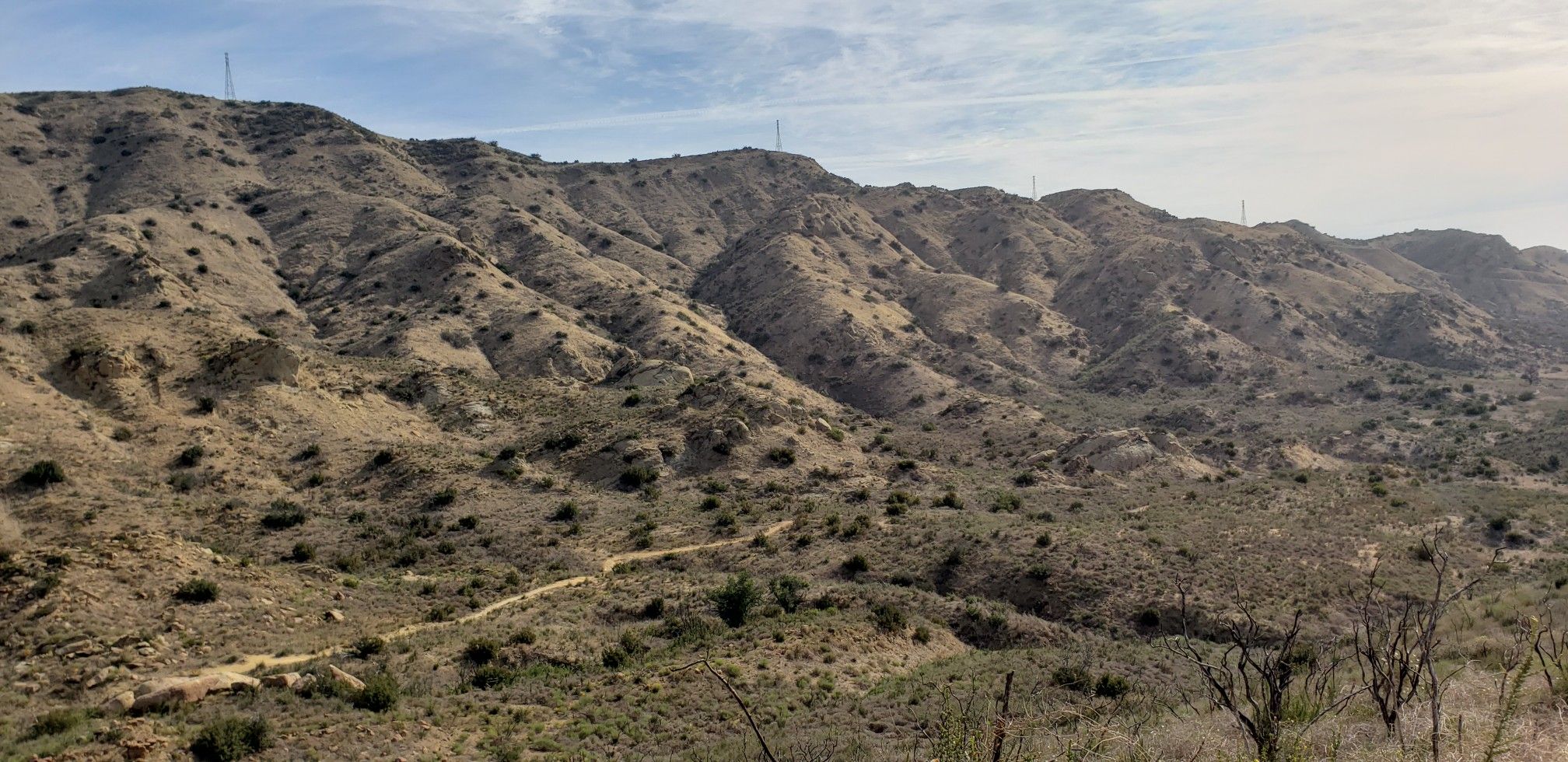 A wide view of dry, rugged mountains with a winding dirt path below. - Cheeseboro and Palo Comado Canyons Loop