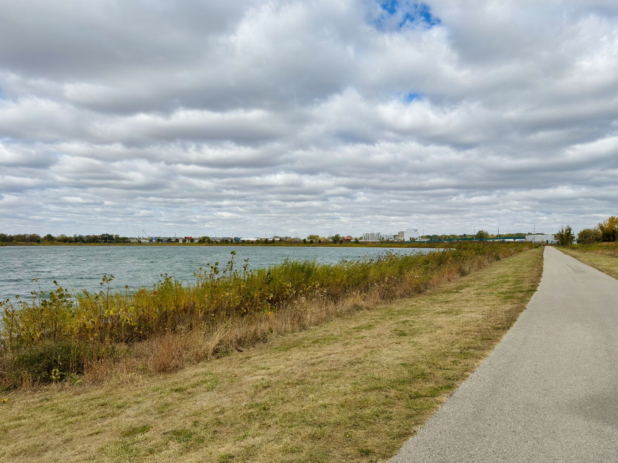 Paved path next to a lake with a grassy bank under a cloudy sky. - Just Do It Trail – Cascade Lake loop from The Highlands on 19th