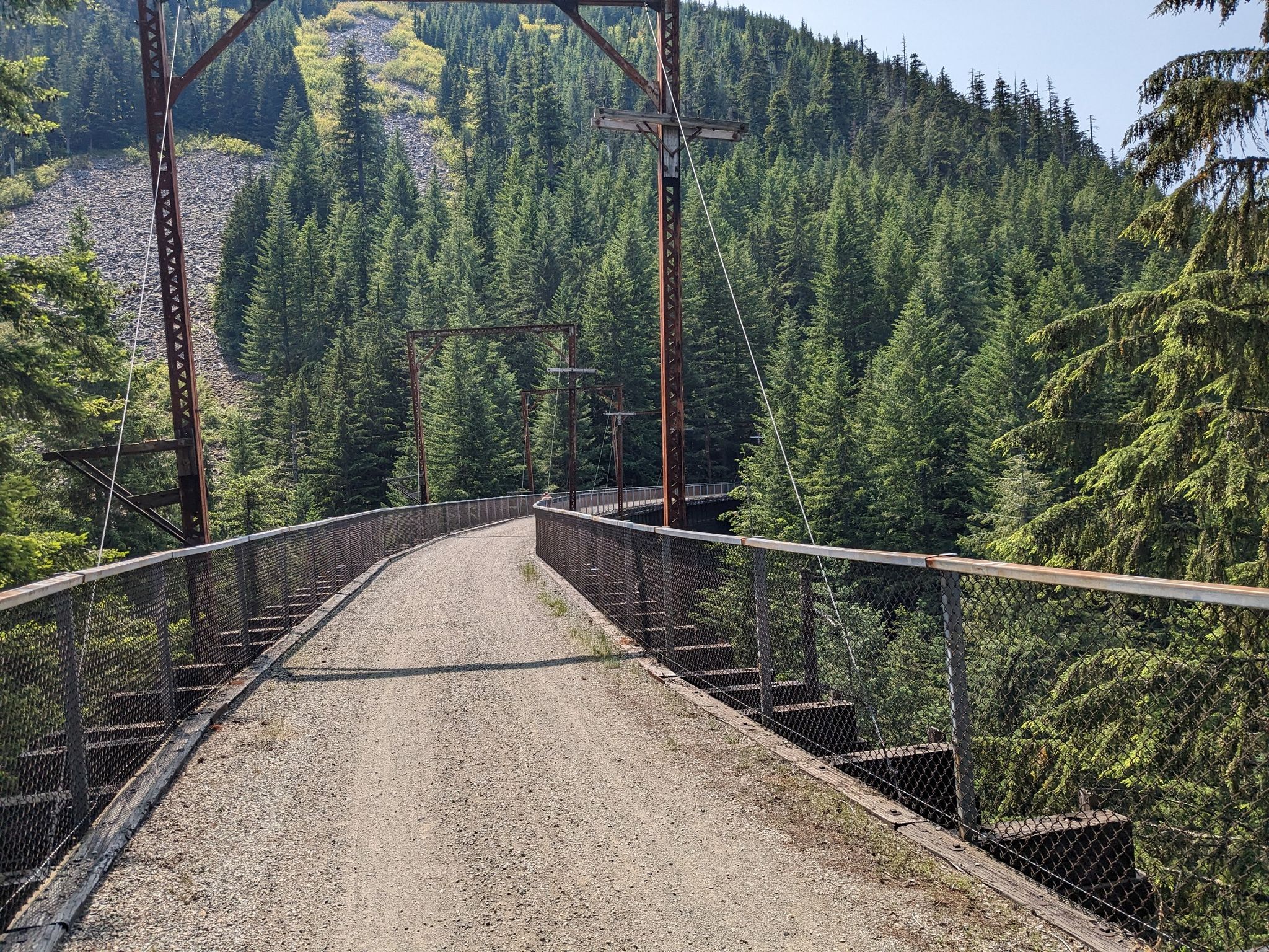 Curved gravel path on a metal bridge over a dense evergreen forest. - Snoqualmie Tunnel – Snoqualmie Pass loop from Change Peak