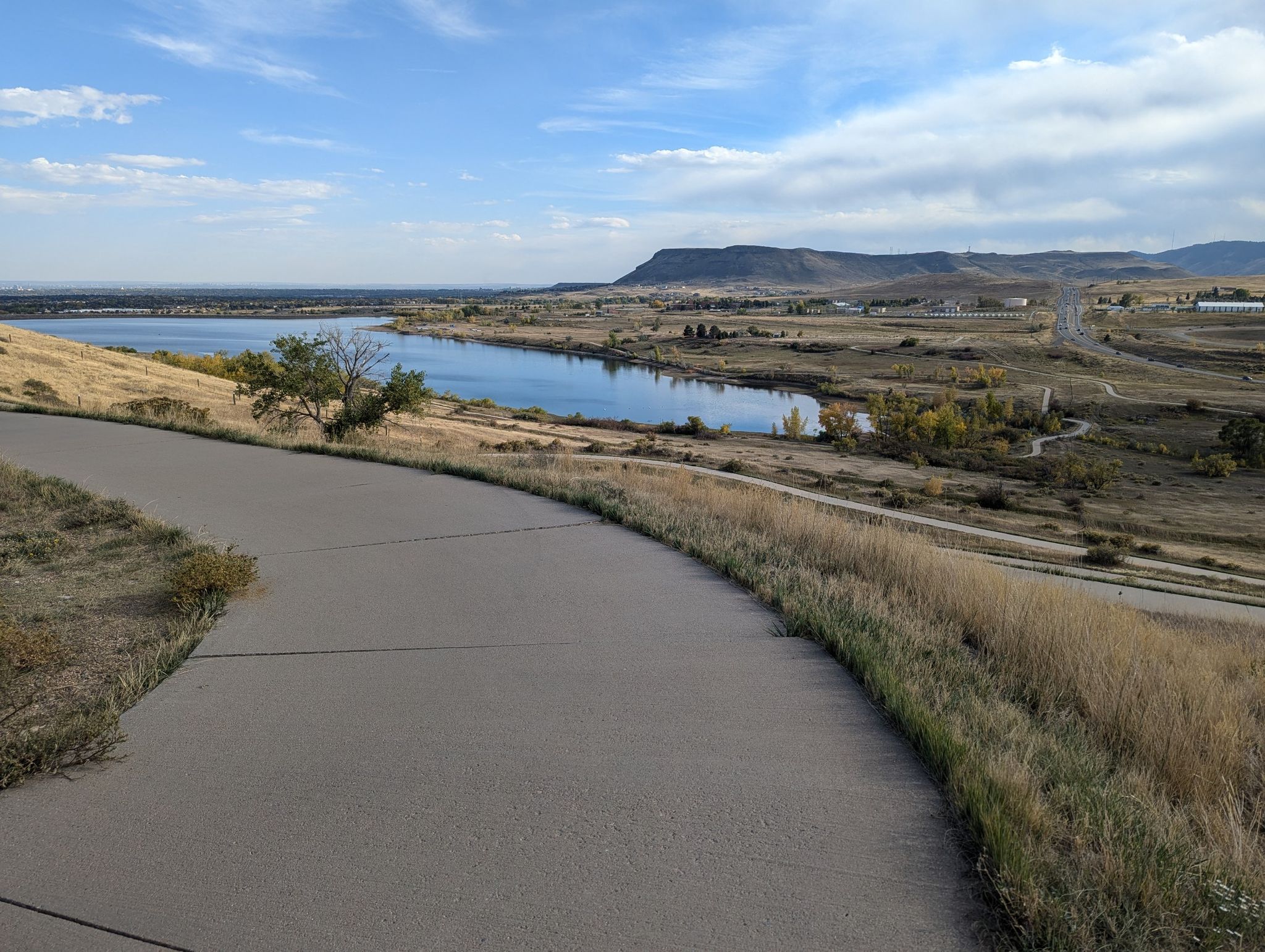 Paved path overlooks a lake and dry hills under a bright, cloudy sky. - Bridge into Golden – Clear Creek Trail loop from 60th & Sheridan - Arvada Gold Strike
