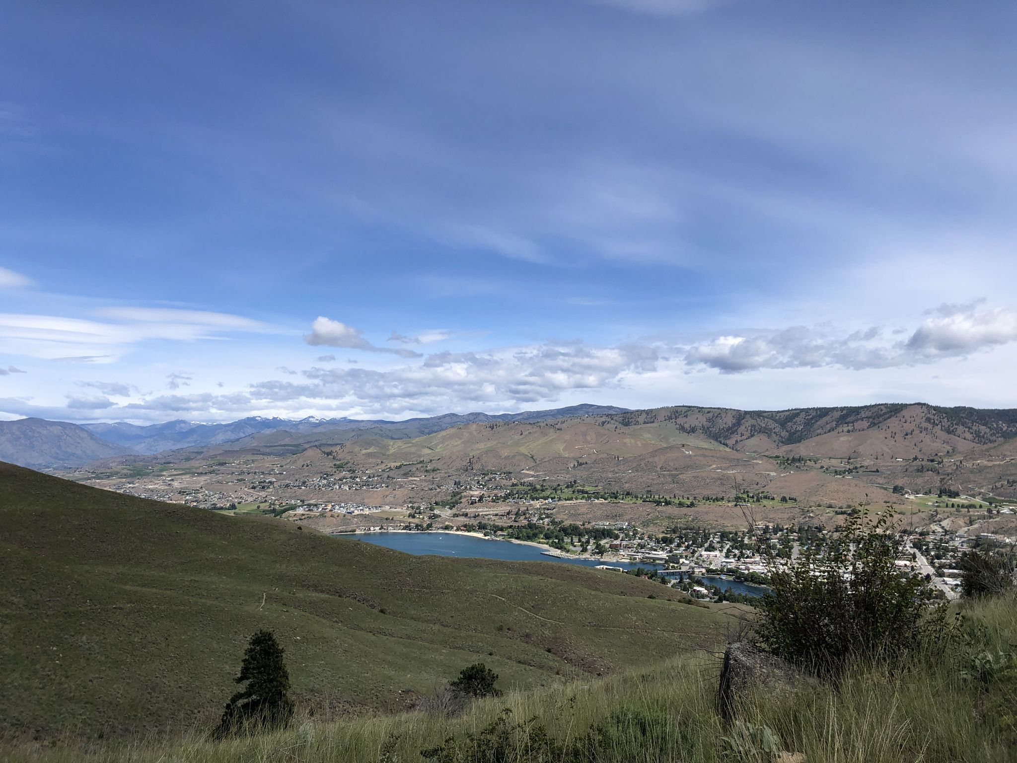 Sunny view of a town and lake in a wide valley, with green hills. - Chelan Butte Trail