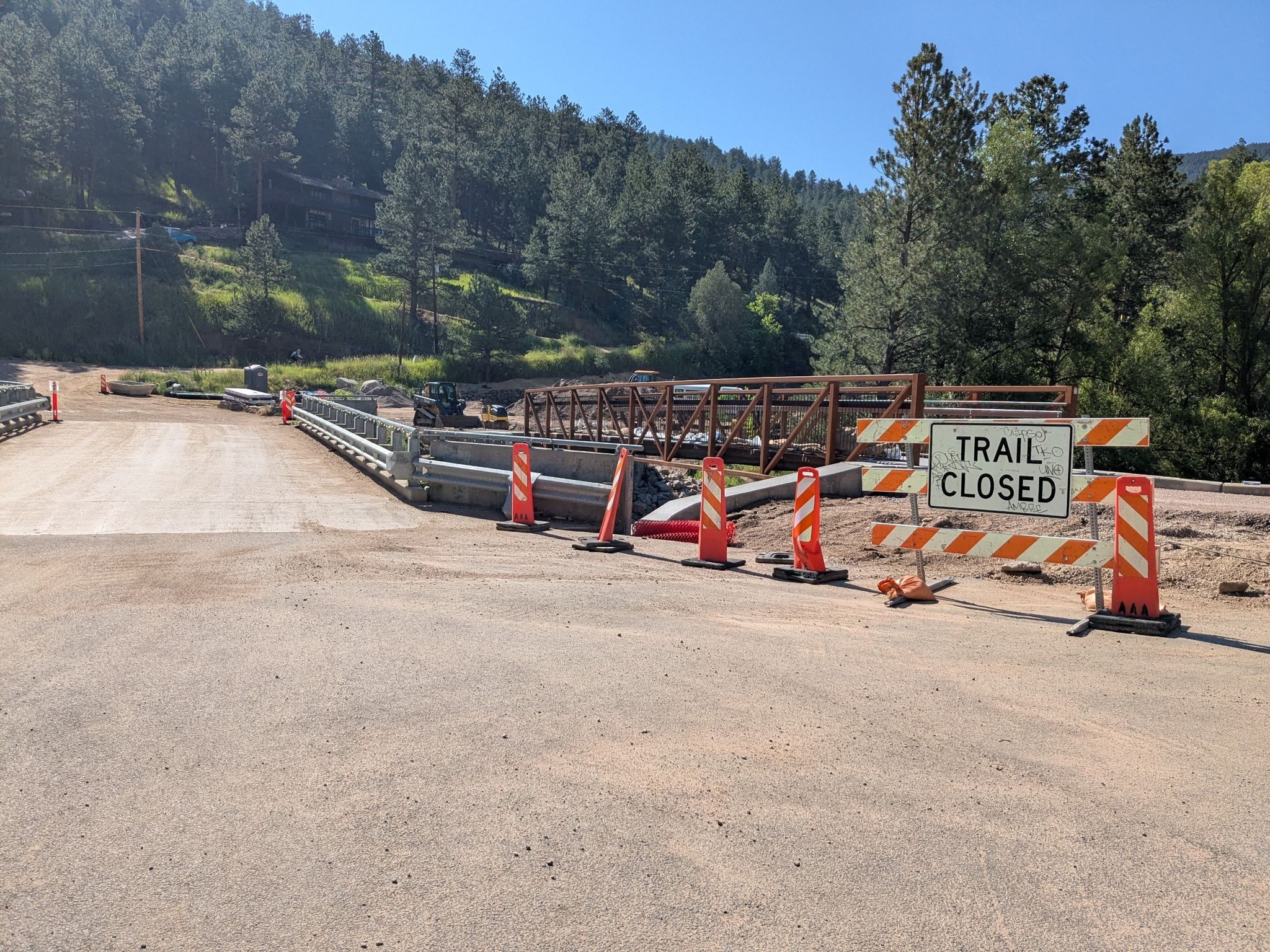 Trail closed sign at a construction site with a new bridge and forested hills. - Boulder Canyon Drive