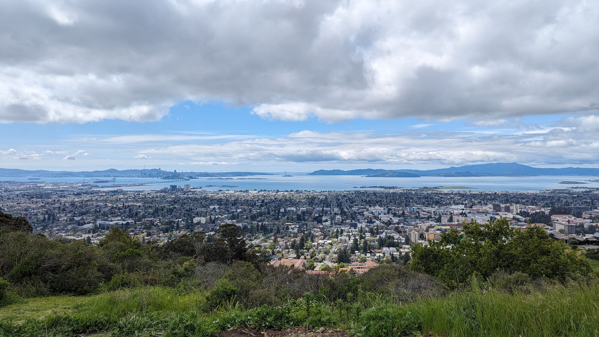 Overcast panoramic view of a city and bay from a green hill. - Stonewall Panoramic Loop