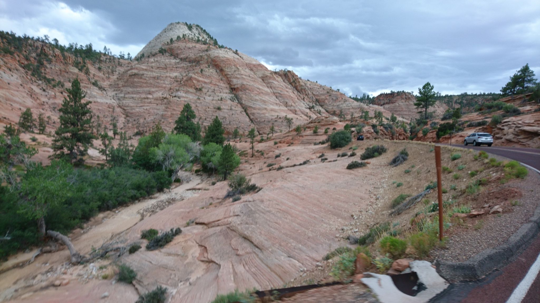 A car drives on a road beside a large, layered sandstone mountain. - The Zion Mount Carmel Tunnel East Entrance from Zion Mountain Ranch
