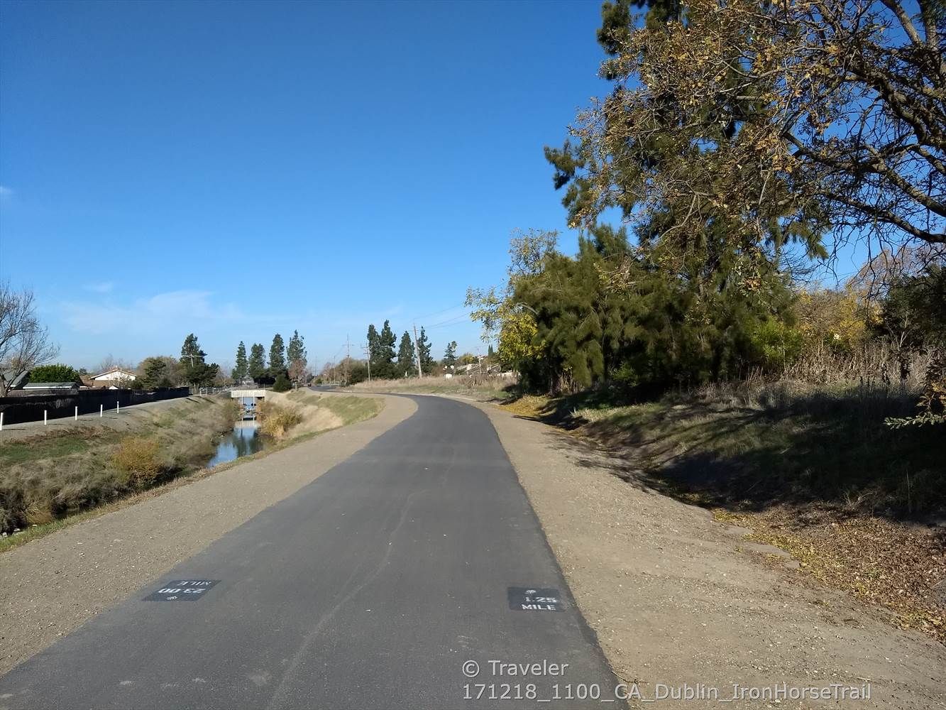 A paved path curves alongside a canal with trees under a clear blue sky. - Iron Horse and Tassajara Loop
