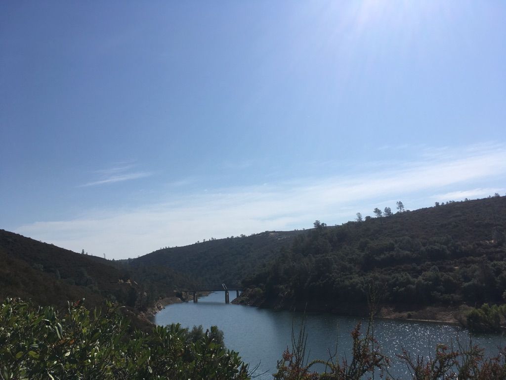 A lake winding through forested hills with a distant bridge under a bright sky. - Acorn Creek Trail loop from Brush Creek Ranch