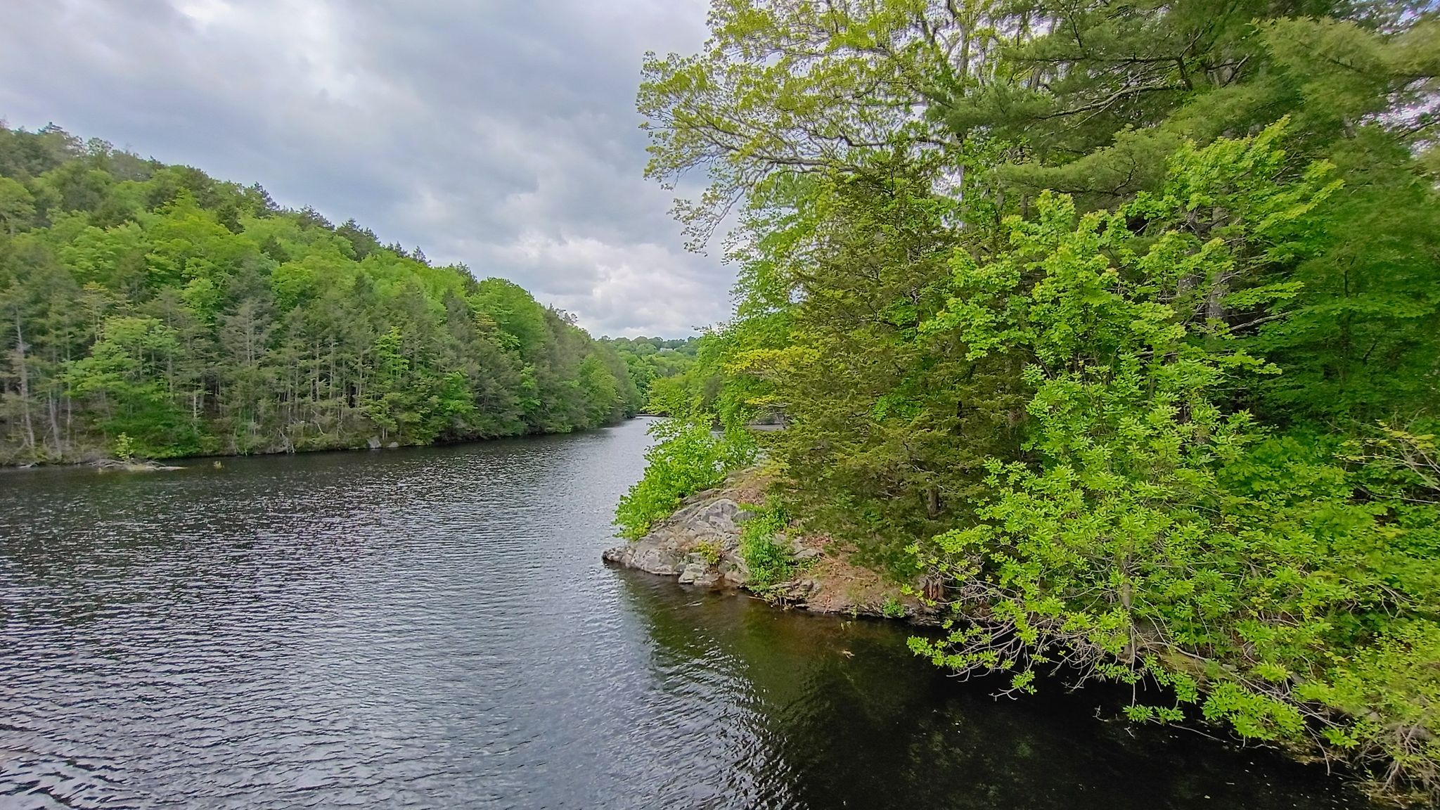 A wide river flows between lush green forested banks under a cloudy sky. - View of Saugatuck Reservoir – View of Saugatuck Reservoir loop from Noroton Heights