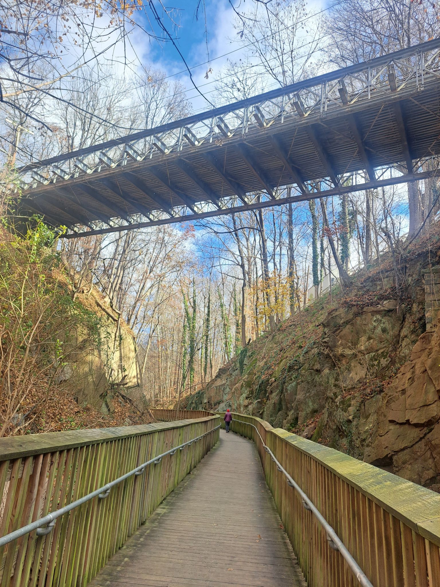 Elevated wooden walkway under a large bridge, person walking in distance. - Starting Point – Trolley Line #9 Trail loop from Ellicott City