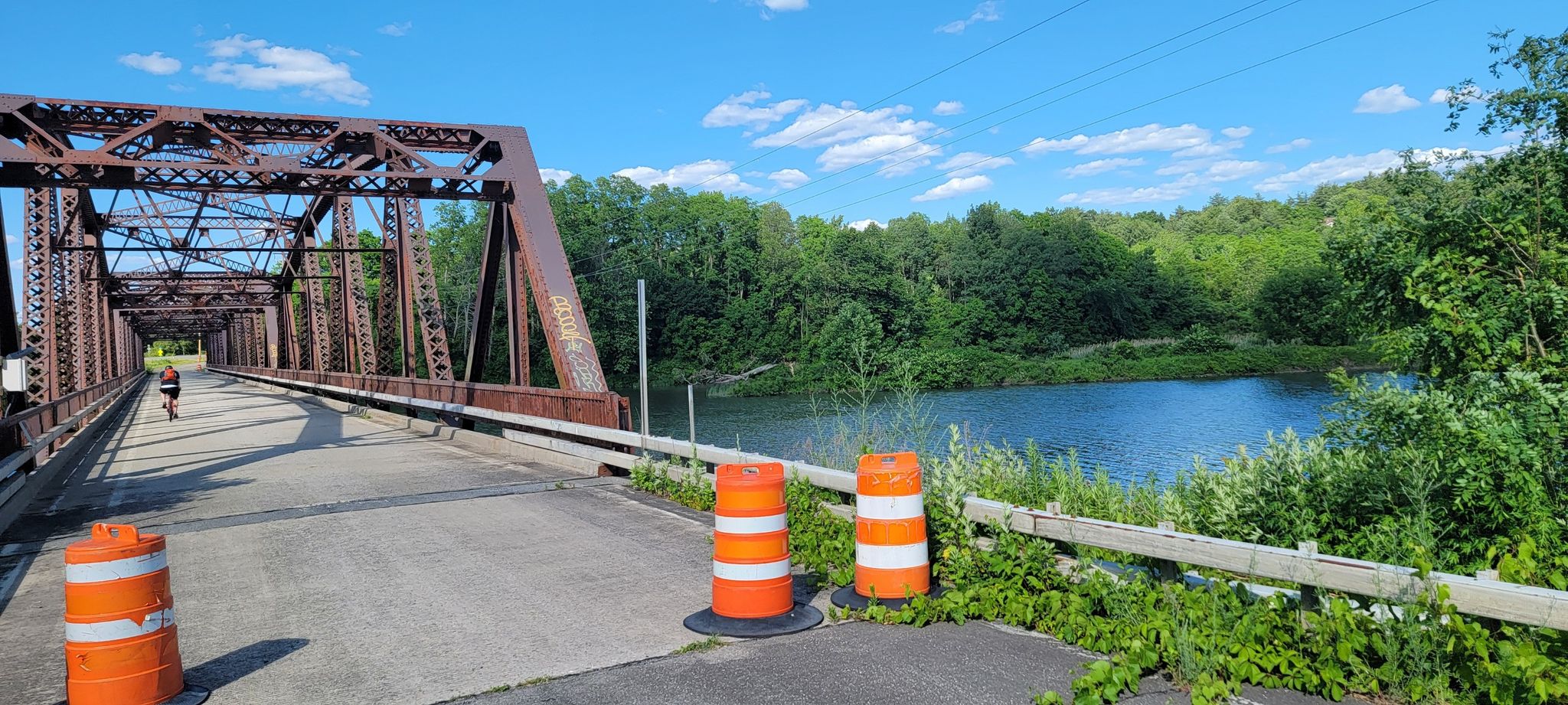 Cyclist on a metal truss bridge over a river, with orange barrels. - Highwheeler Coffee – Fort Klock loop from Amsterdam