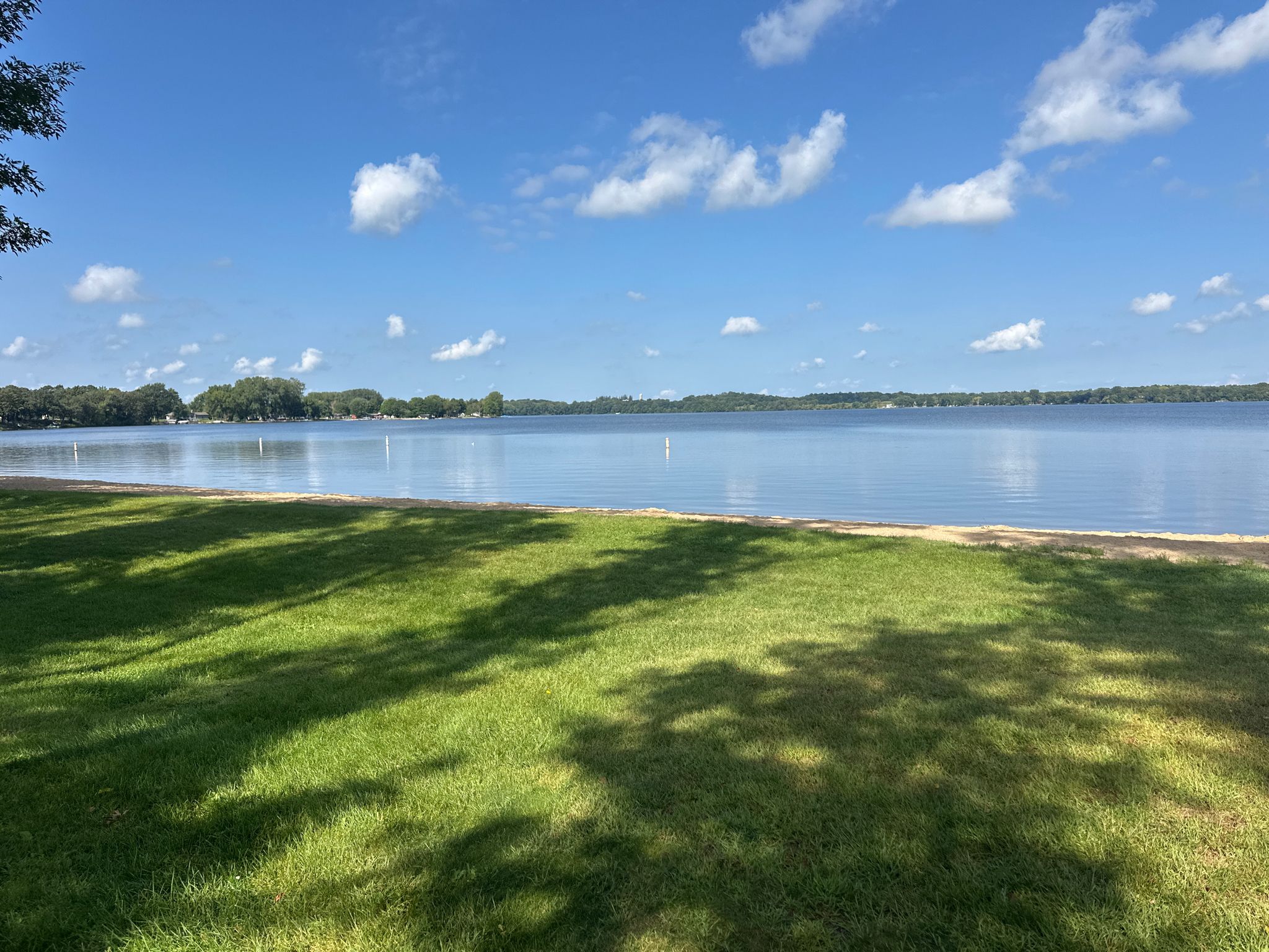 Grassy lawn overlooking a calm lake under a blue sky. - Cannon Lake beach – Cannon Lake loop from Faribault