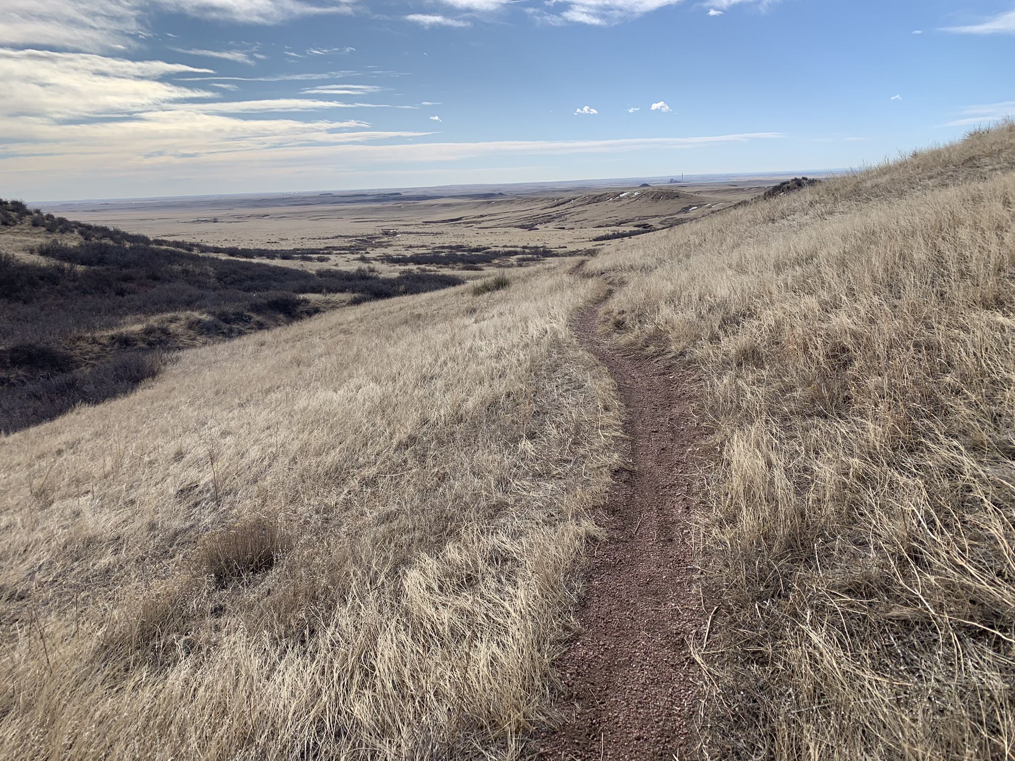 A dirt trail winds through dry, golden hills under a bright sky. - Horse water tank loop from Lindenmeier Overlook