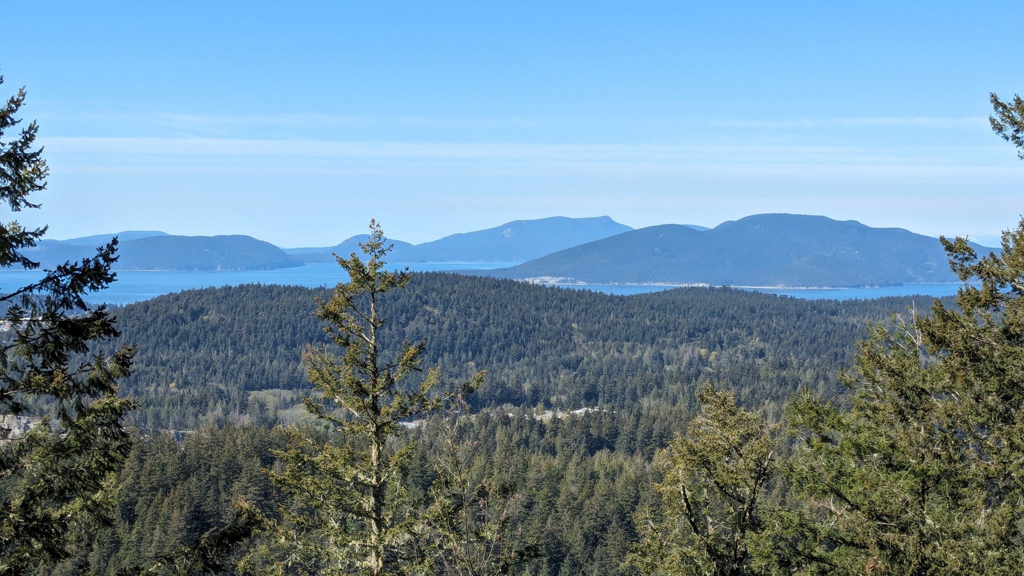 View of forested hills and distant islands across blue water on a sunny day. - Mount Erie & Sugarloaf loop