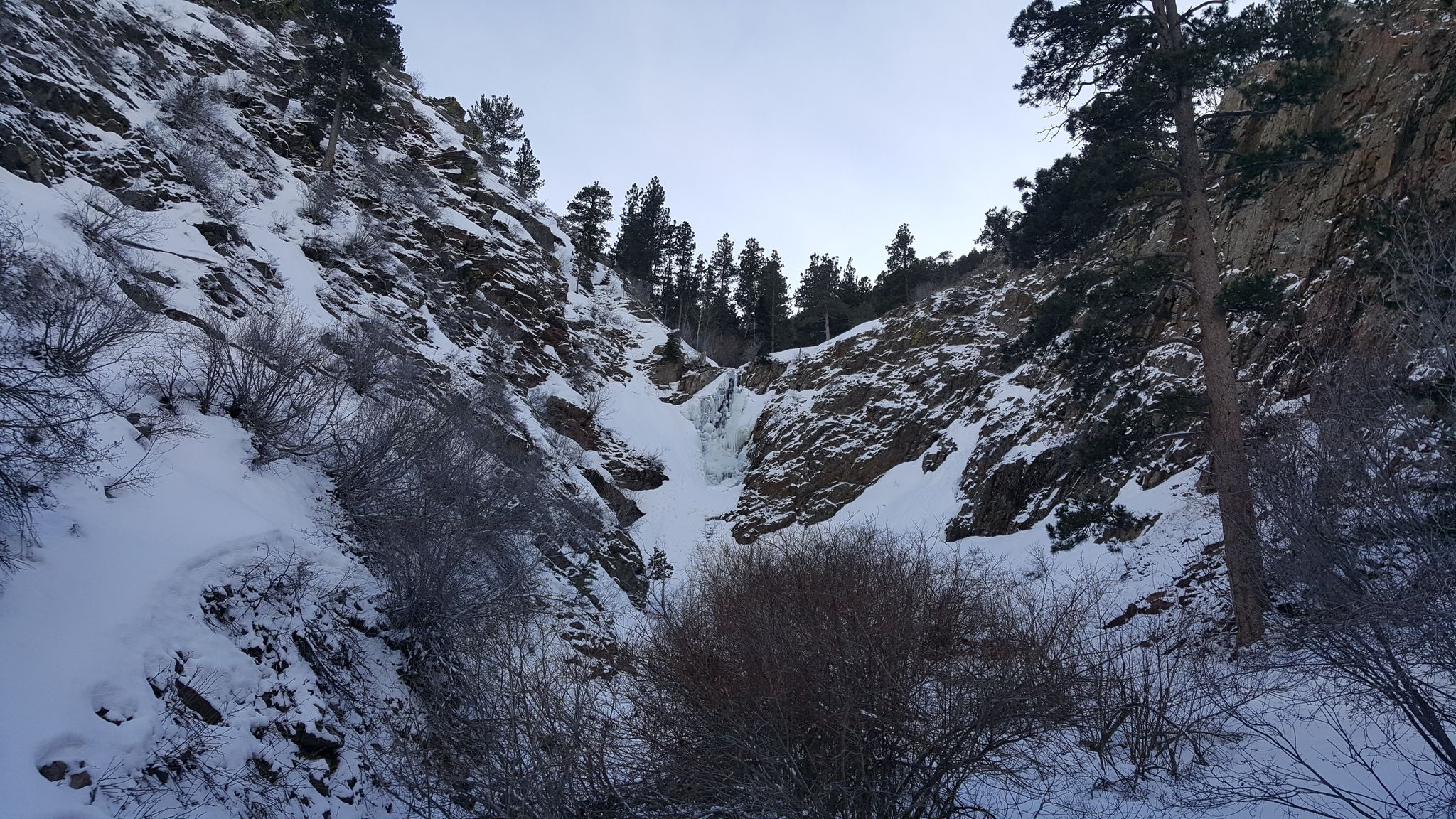 A frozen waterfall cascades down a snowy, rocky canyon under a winter sky. - Garden Creek Waterfall Loop