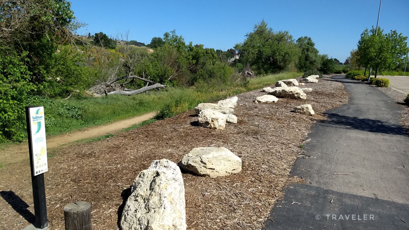 A paved path lined with large white rocks and a signpost on a sunny day. - Lawrence Moore Park loop from Stoney Creek Rd at Dry Creek Apartments