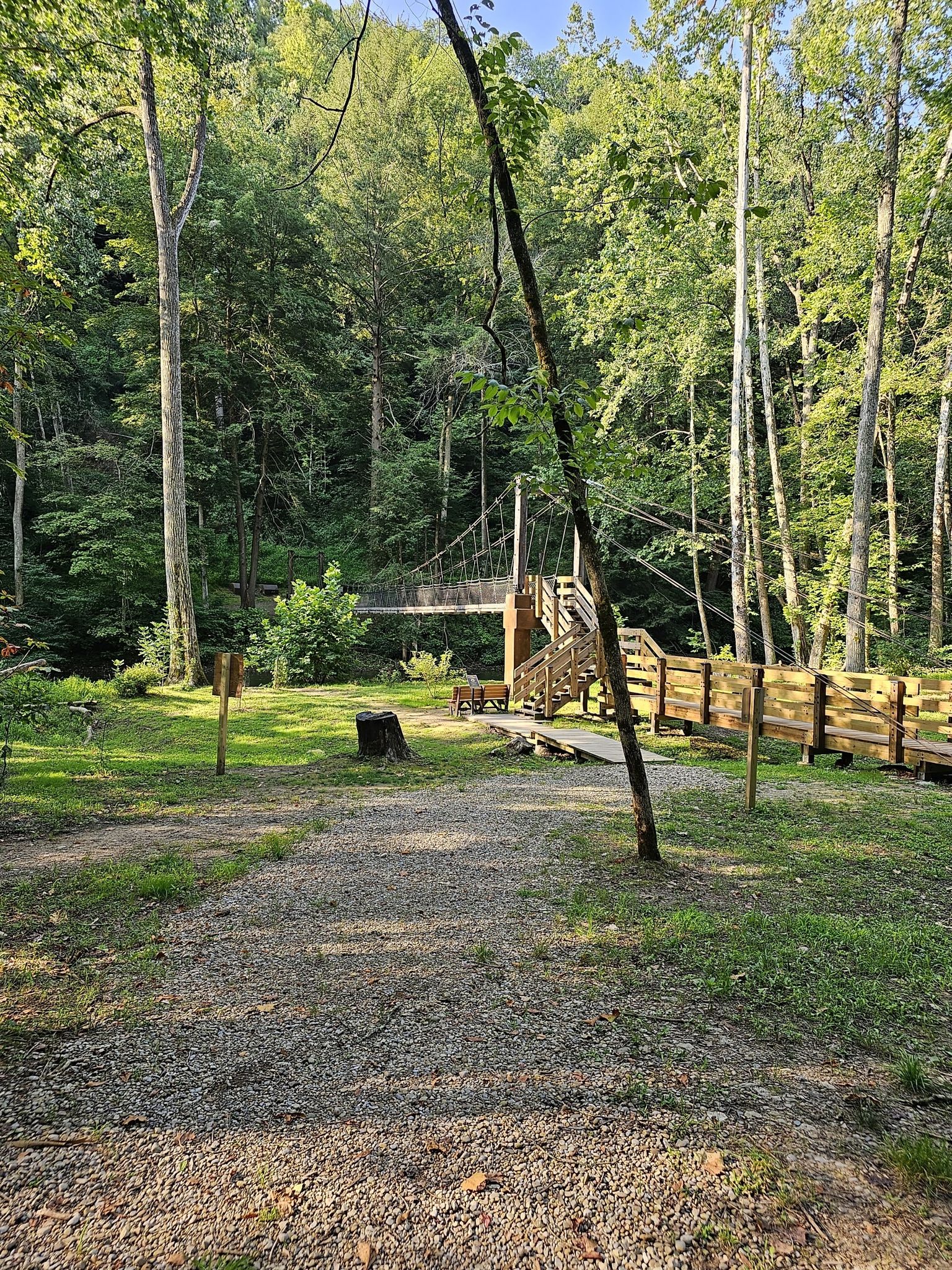 A wooden suspension bridge entrance in a sunny, grassy forest clearing. - Hemlock Gorge and Lyons Falls Trail