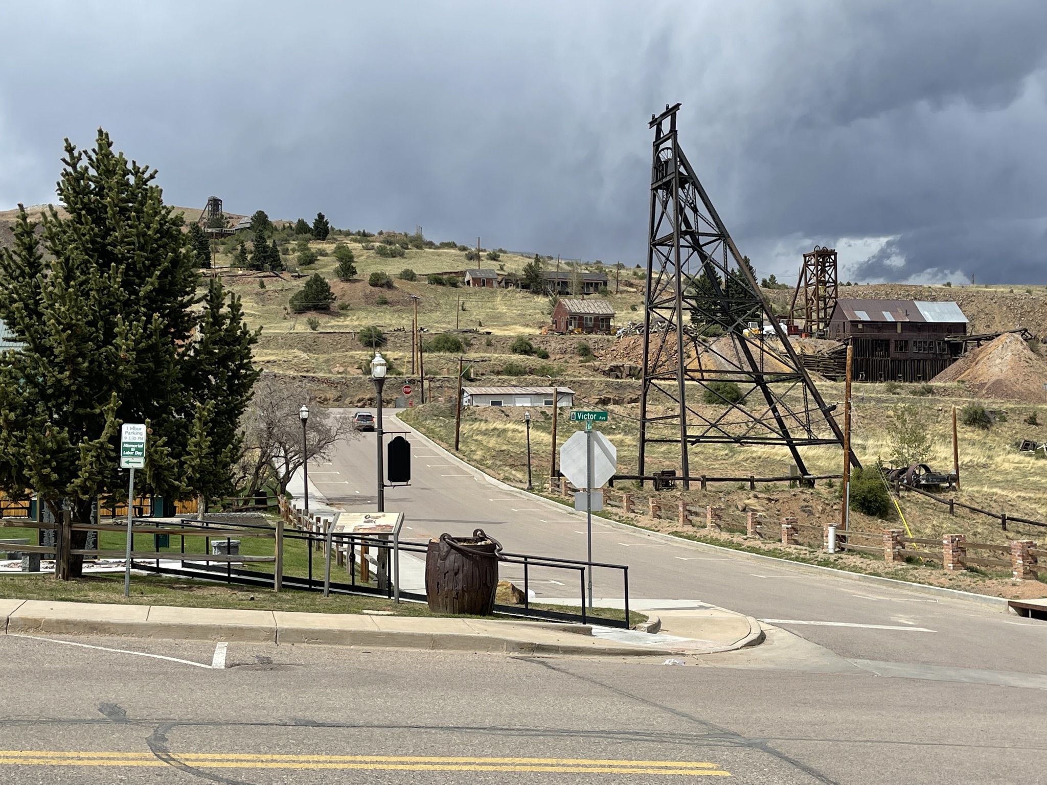Overcast view of a street corner with a large mining headframe and hilly landscape. - Start of Phantom Canyon Road – View of Victor loop from horse trailer parking