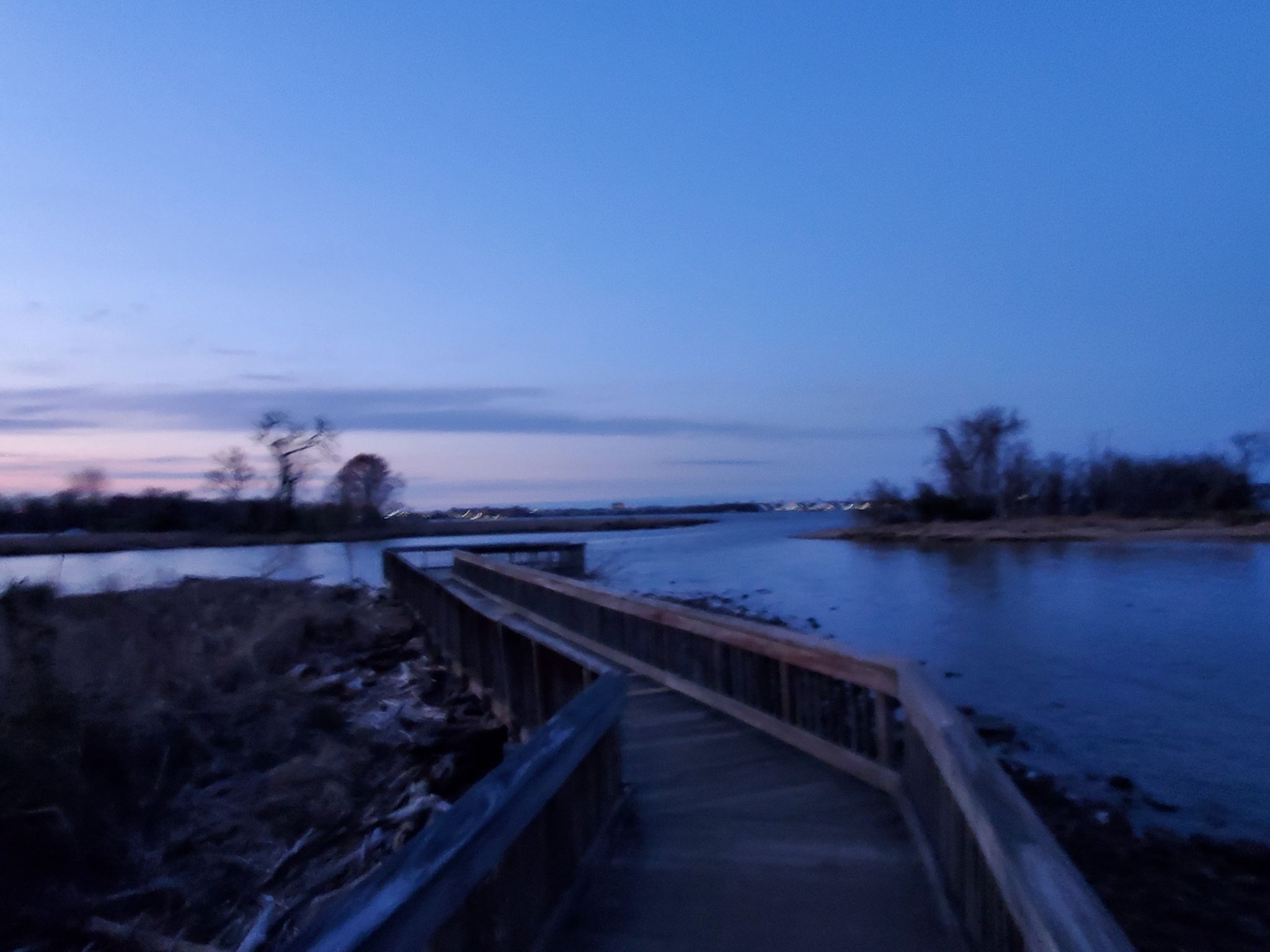 Wooden boardwalk extending over dark water under a deep blue twilight sky. - Mount Vernon Trail and Dyke Marsh Haul Road Trail