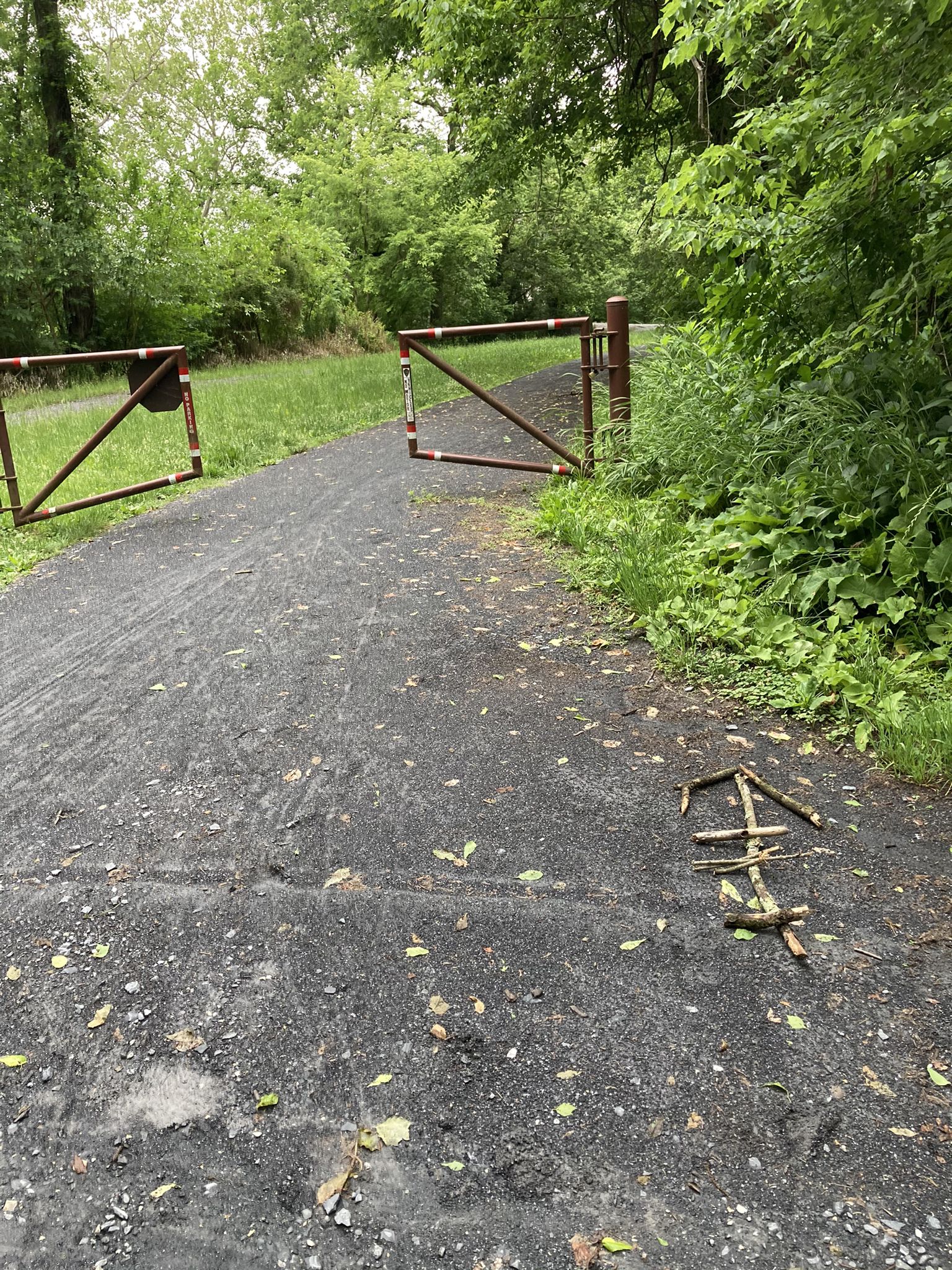 Two rusty metal gates blocking a paved path in a grassy, wooded area. - Gravel loop from Monocacy Aqueduct