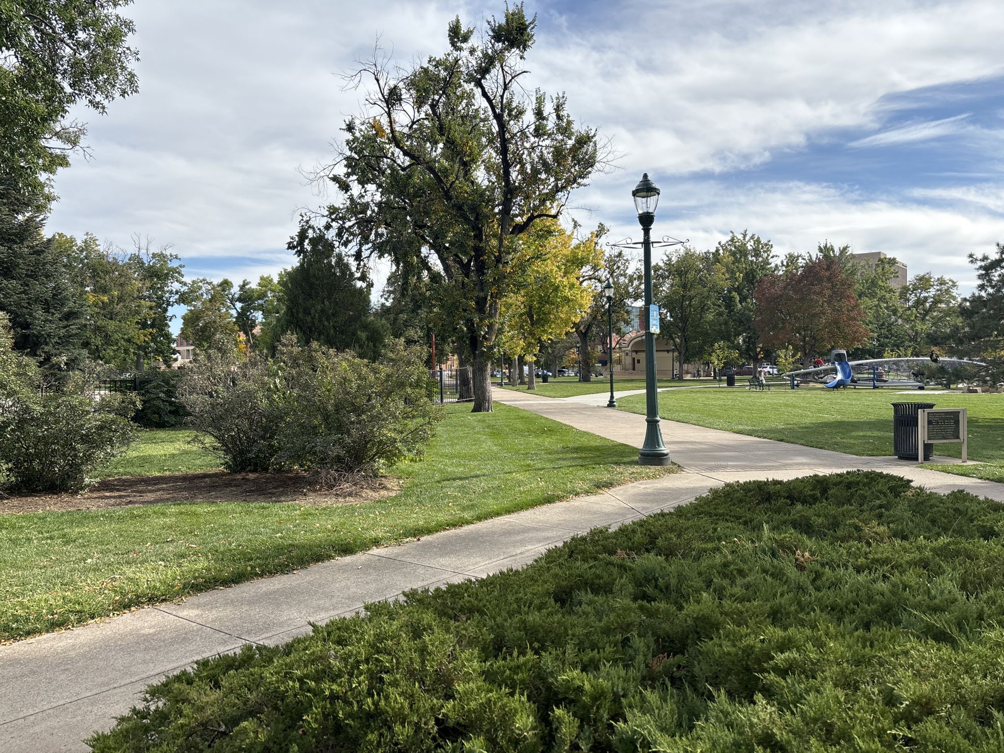A paved park path winds through green grass and trees under a partly cloudy sky. - Downtown Colorado Springs and Colorado College loop