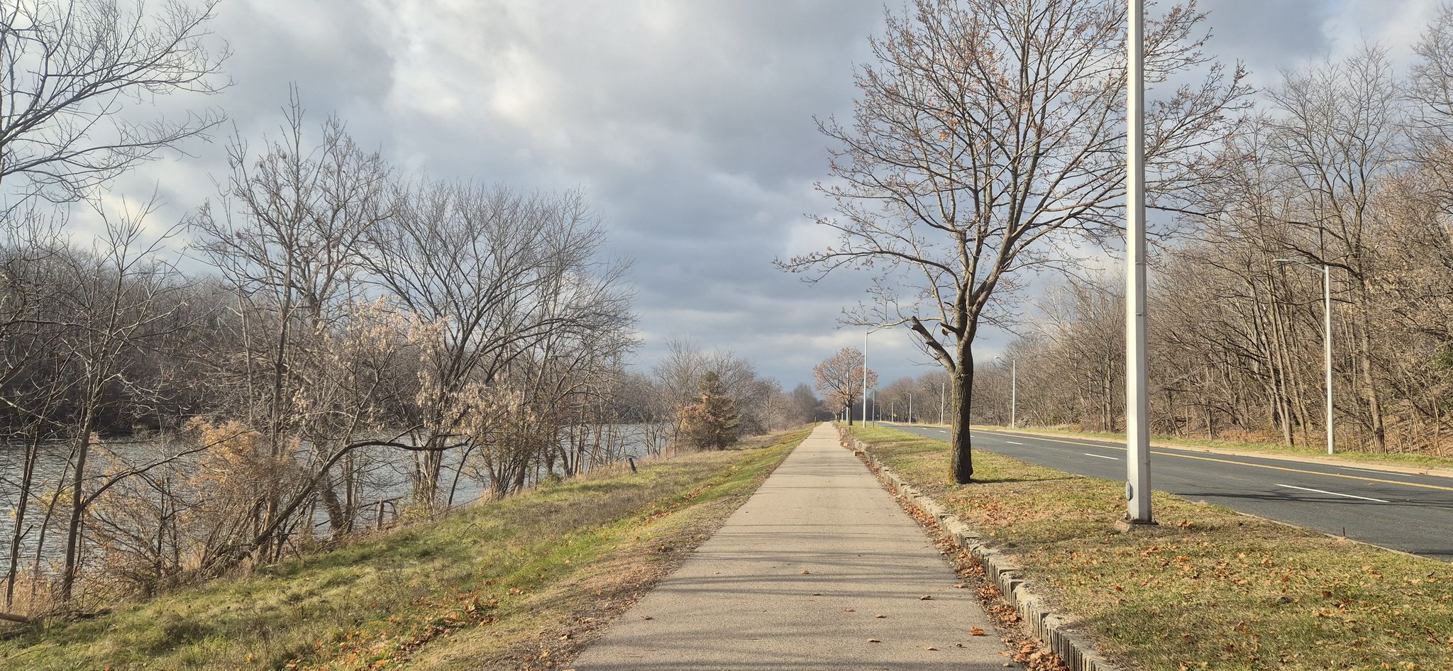 Paved path next to a river and road, under a cloudy sky. - Kalamazoo River loop from Kellogg Community College