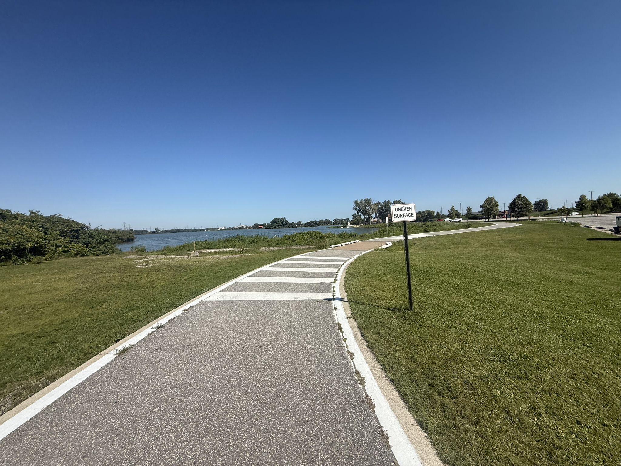Paved path with white stripes curving by a lake under a clear blue sky. - 18th Street Brewery loop from Hammond-Whiting