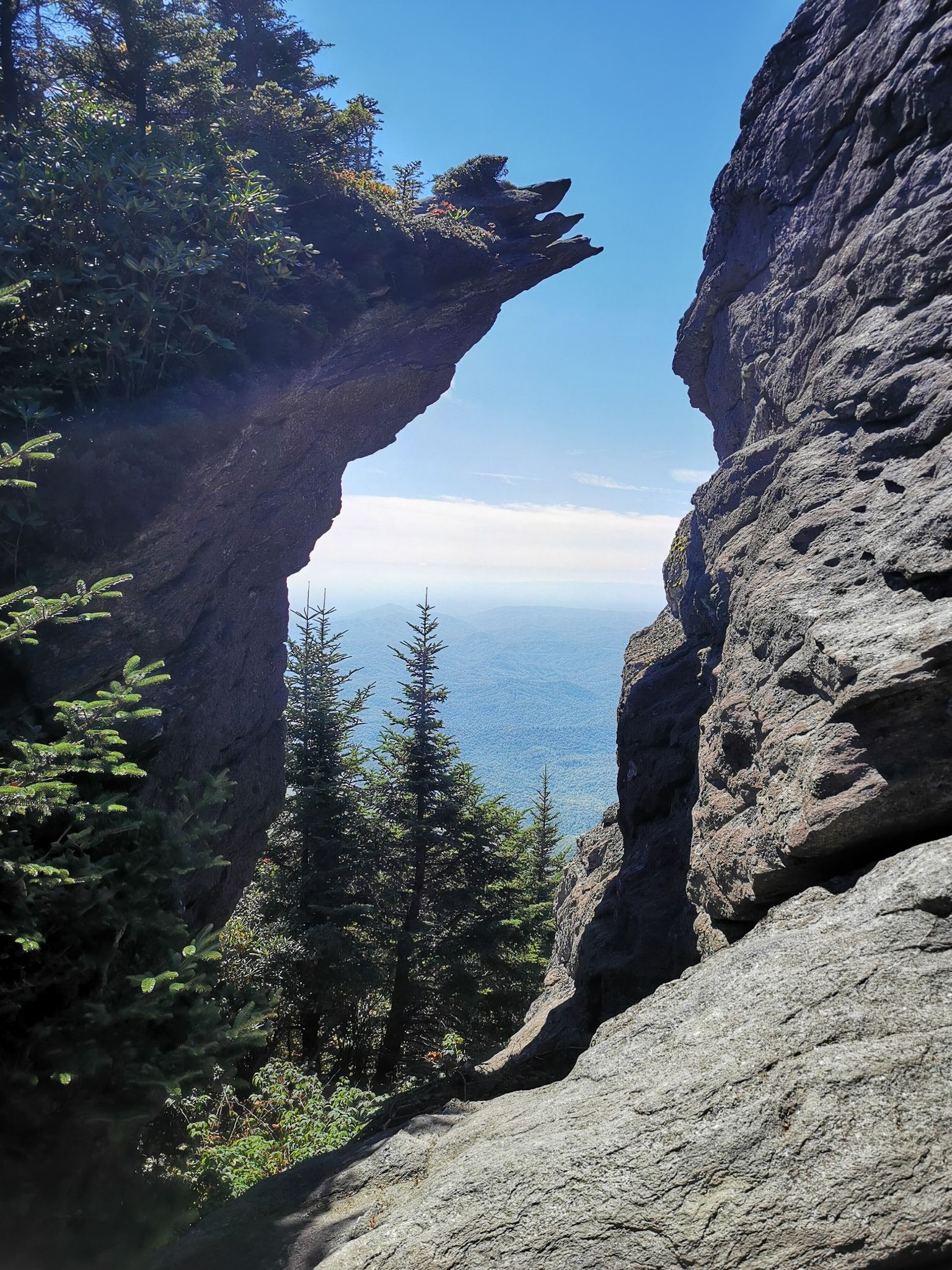 Narrow rock crevice opening to a distant mountain view under a clear sky. - Grandfather Trail