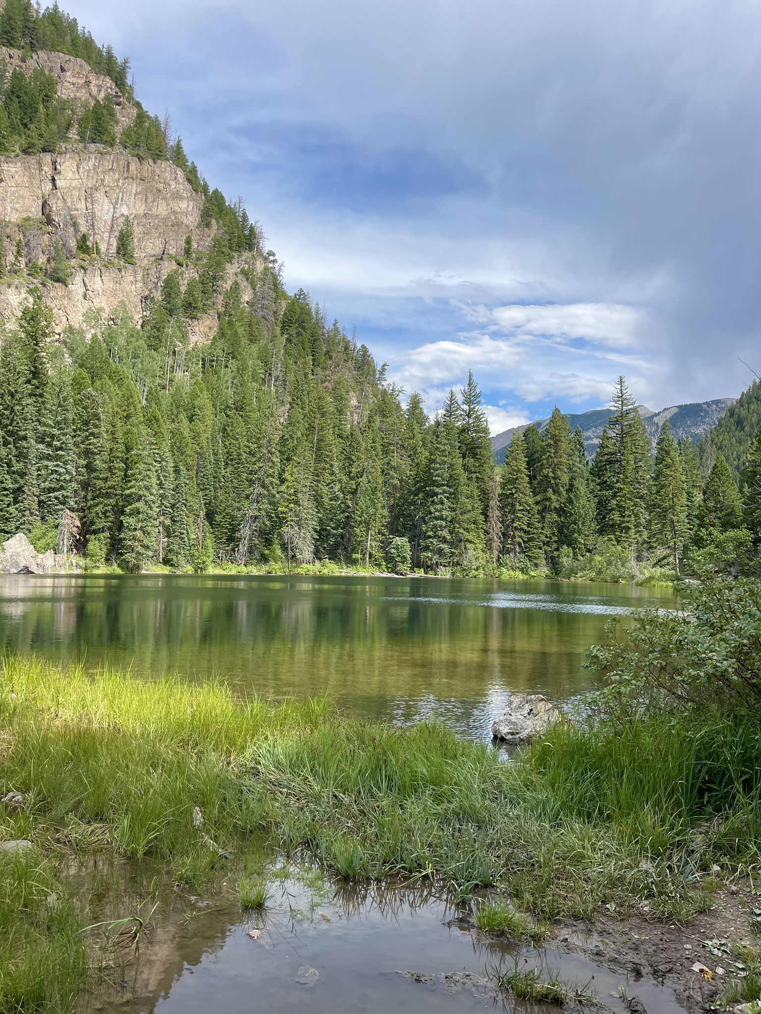 Serene mountain lake surrounded by lush green forest under a cloudy sky. - Crystal City Road #314