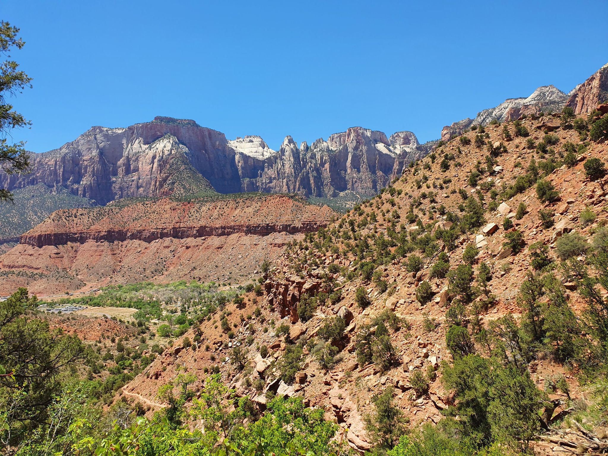 Vast desert landscape with red rock hills, green scrub, and distant mountains under blue sky. - Watchman Trail – Zion National Park loop from Springdale