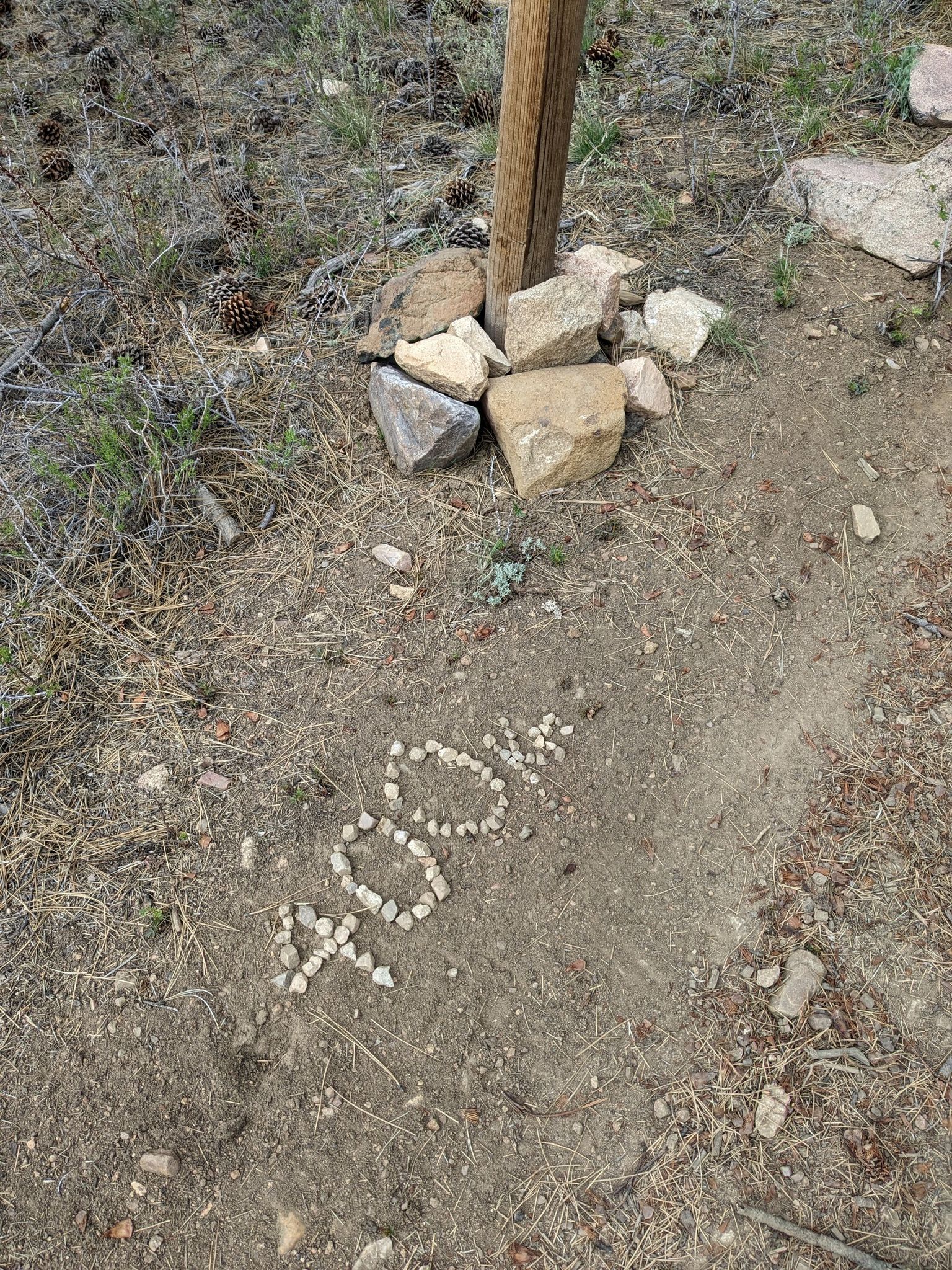 Small rocks spell "400k" on dry ground next to a wooden post. - Wysup Peak Trail