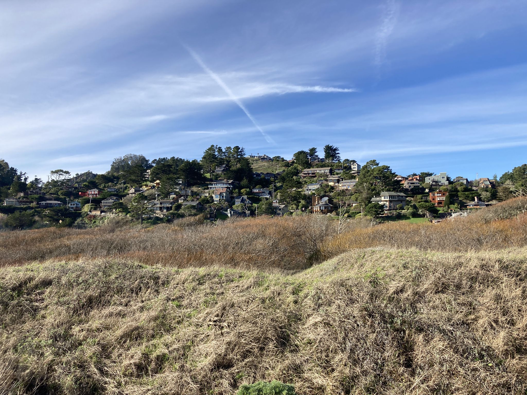 Houses on a distant green hill under a bright blue sky. - Pirate's Cove