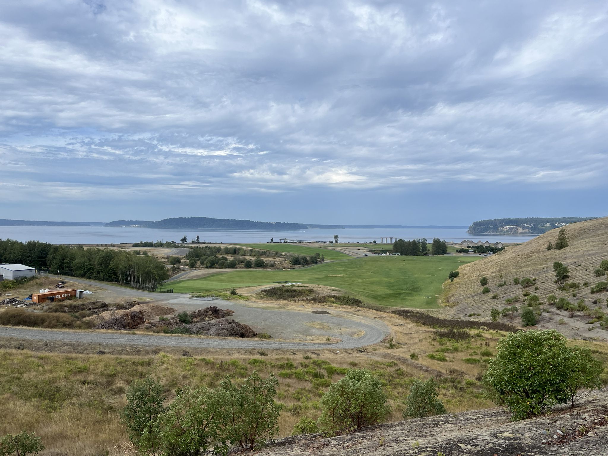 Overcast view of a green golf course, water, and hills under a cloudy sky. - Grandview Trail – Titlow Park loop from Tacoma Community College
