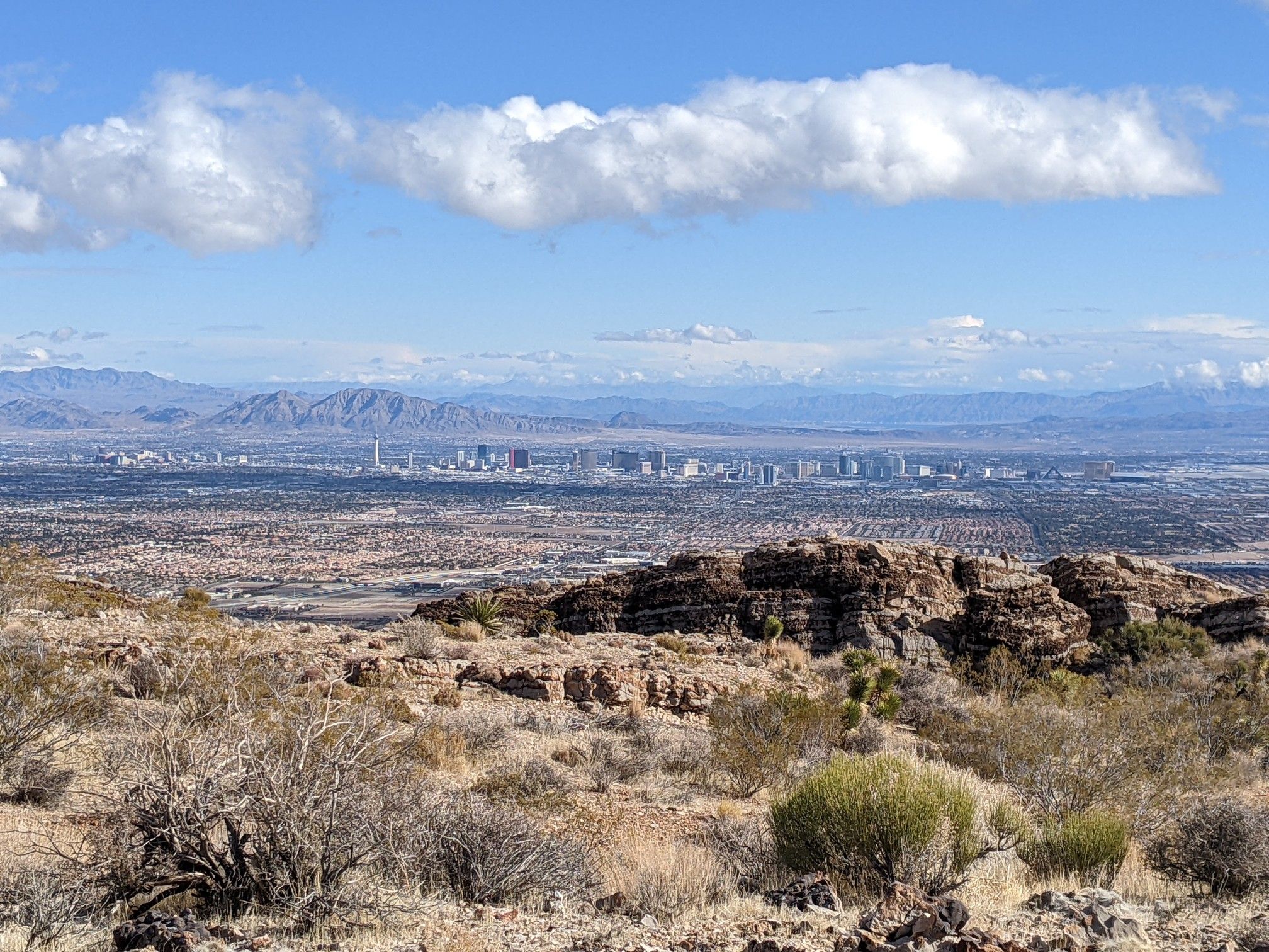 Distant city skyline across a vast desert landscape under a cloudy blue sky. - Cowboy Trails loop