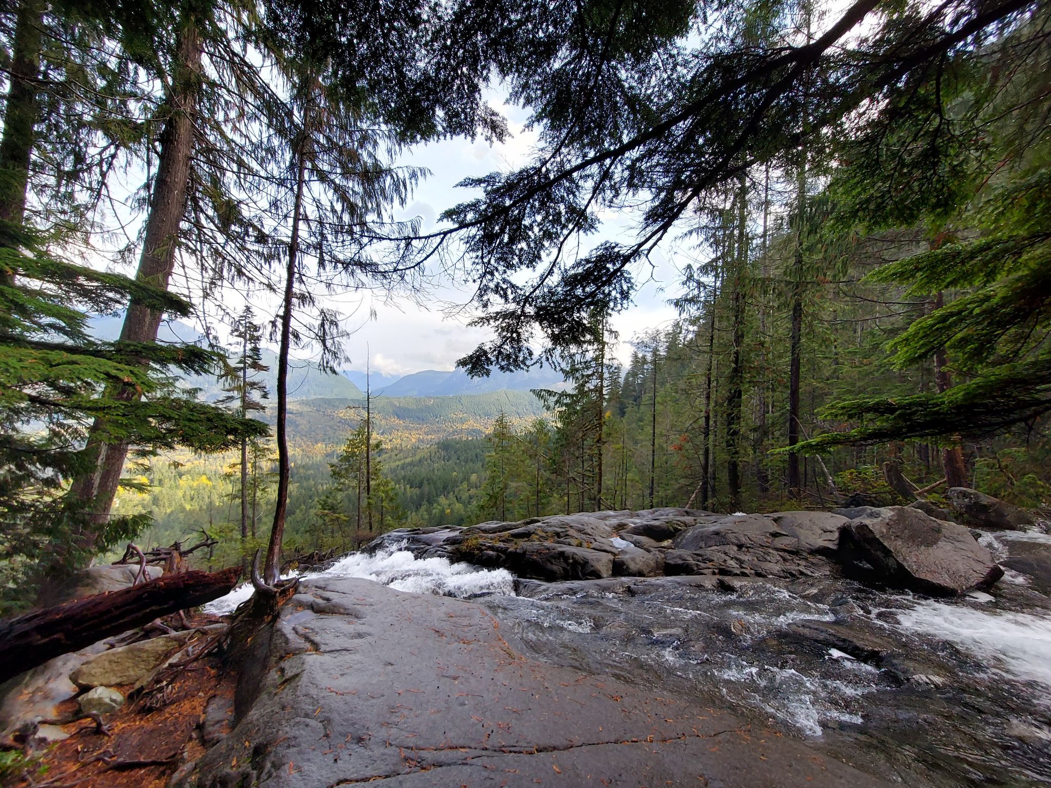 Waterfall cascading over rocks into a lush forest valley under bright skies. - Lake Serene Trail