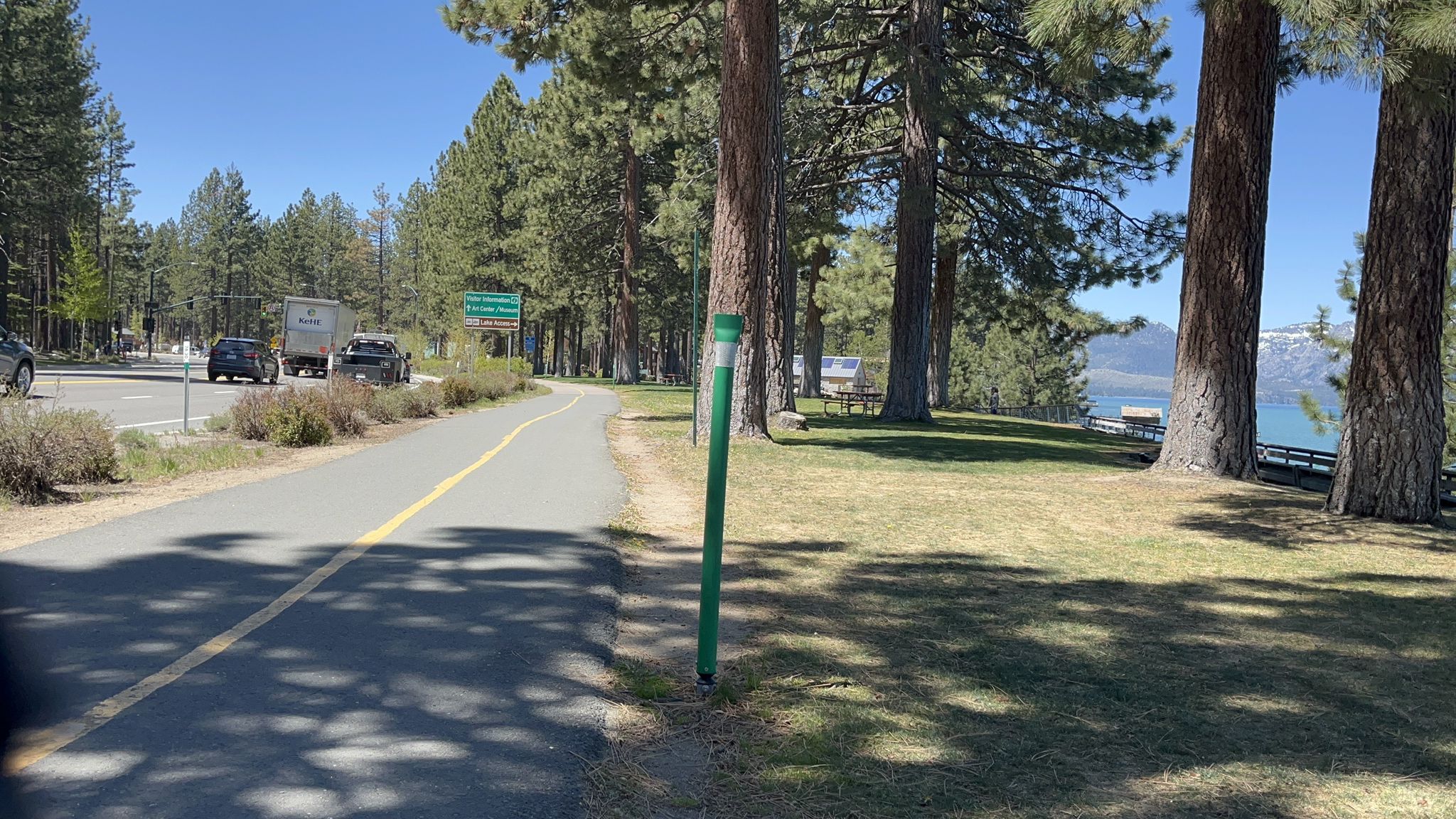 Road and bike path alongside a pine forest with a distant lake. - Stateline-South Lake Tahoe – South Lake Tahoe loop from Van Sickle Bi-State Park