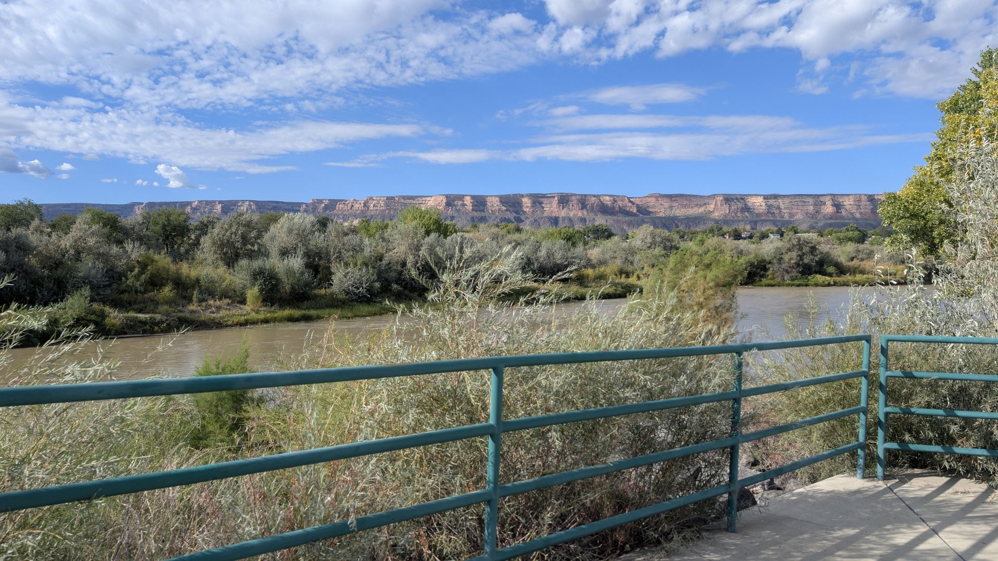 River flowing past green bushes and trees, with distant rocky cliffs. - Over The Edge Sports loop from Truck Parking