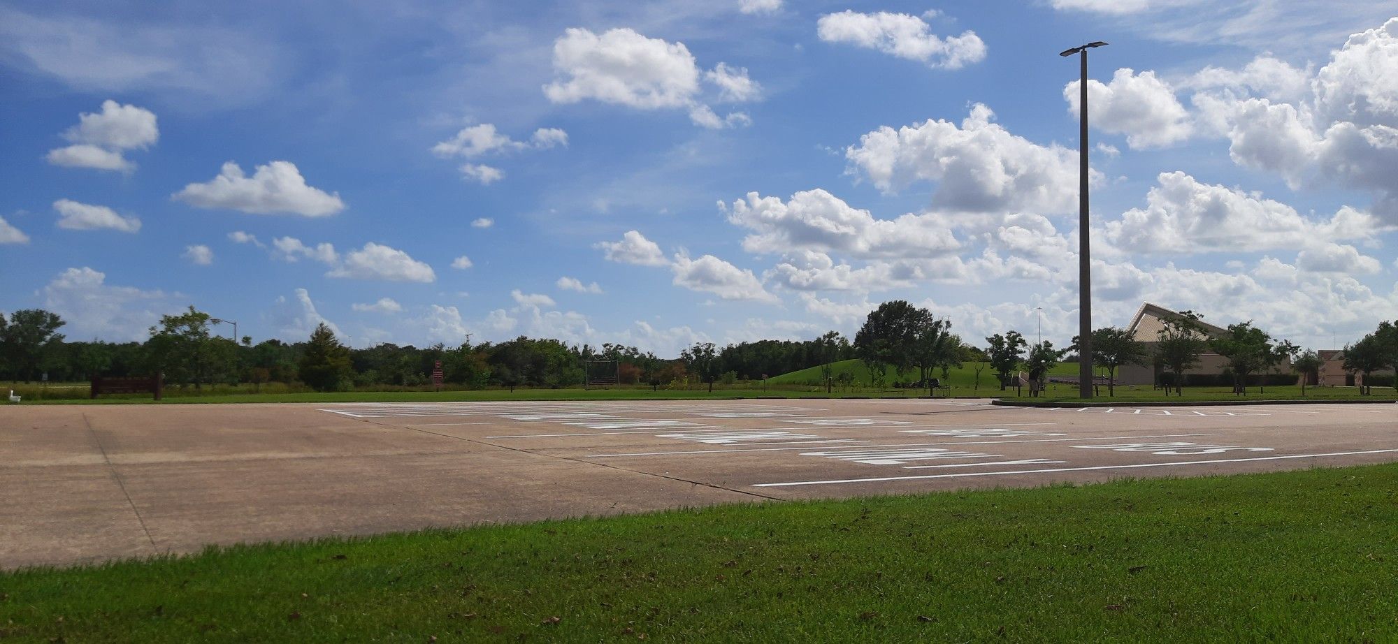 Sunny day over a paved lot, green grass, and distant trees under a cloudy sky. - Tom Bass Section 1 Loop