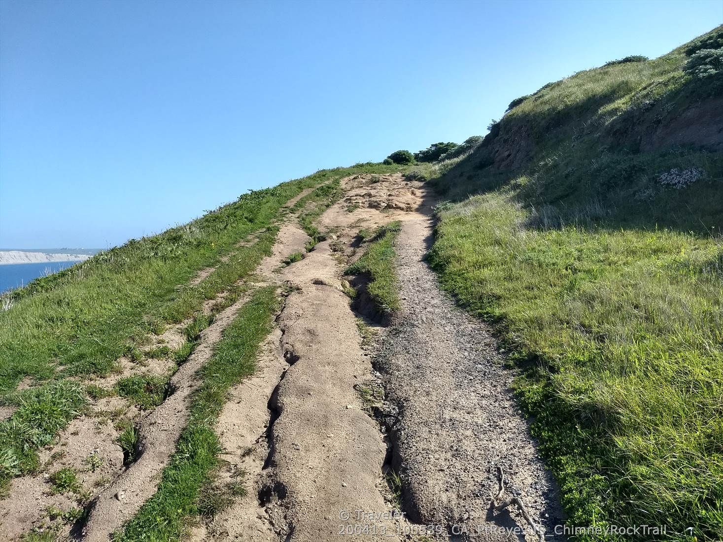 A dirt trail winding up a grassy hillside towards a clear blue sky. - Chimney Rock Trail