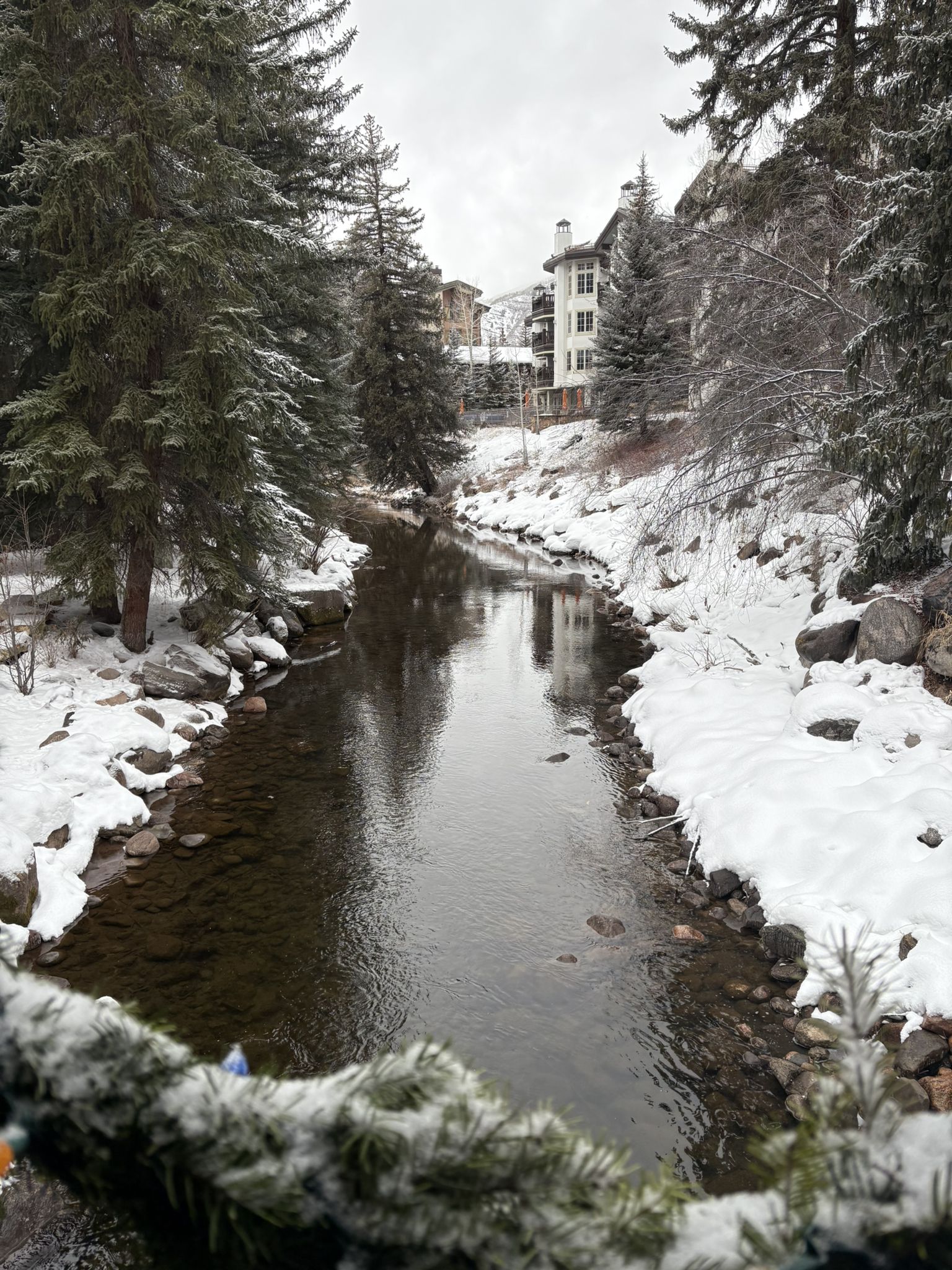 Winter stream flowing through snow-covered banks with pine trees and a building. - Vail loop from Vail