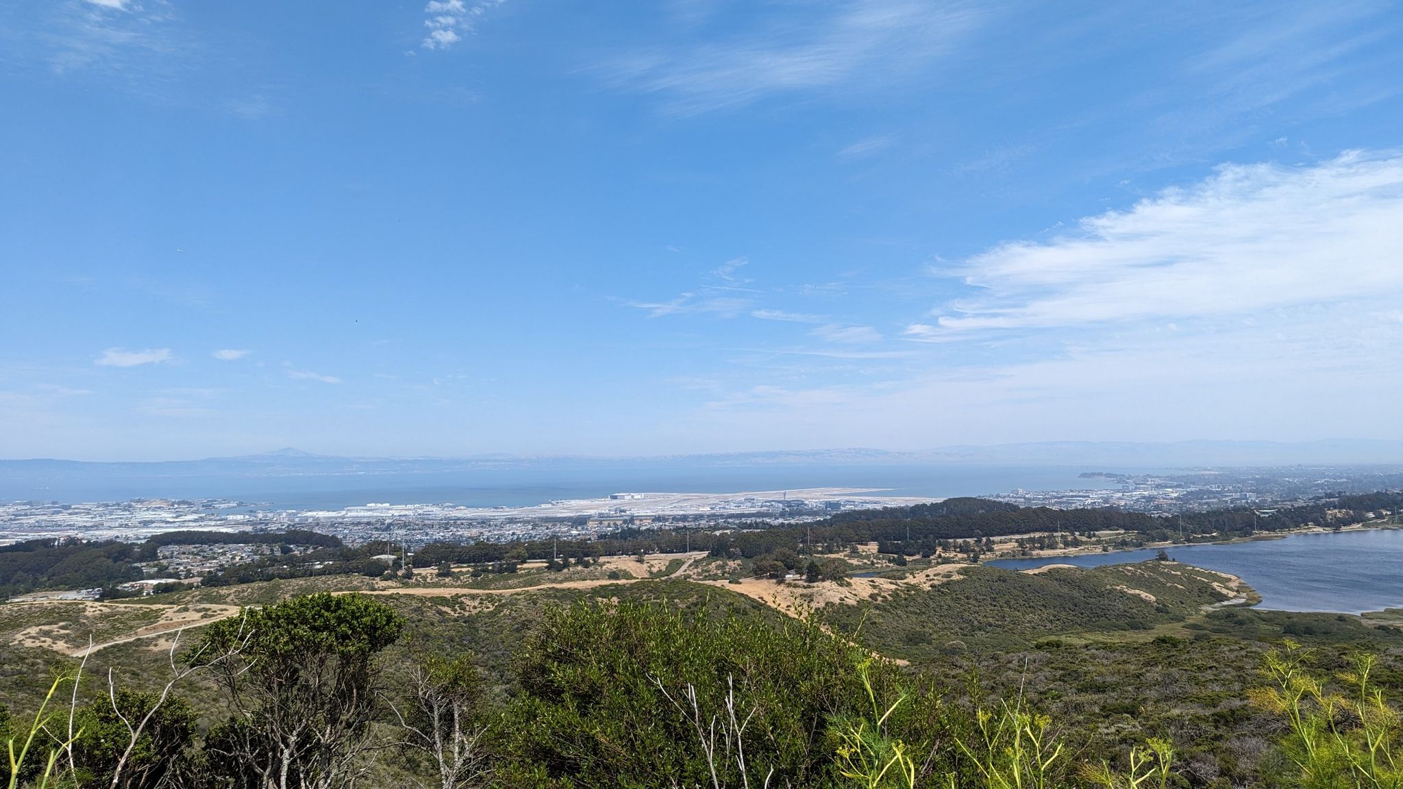 Panoramic view of green hills, a distant city, and a large body of water. - Sneath Lane Trailhead – Nike Missile Site loop from Sweeney Ridge (GGNRA)