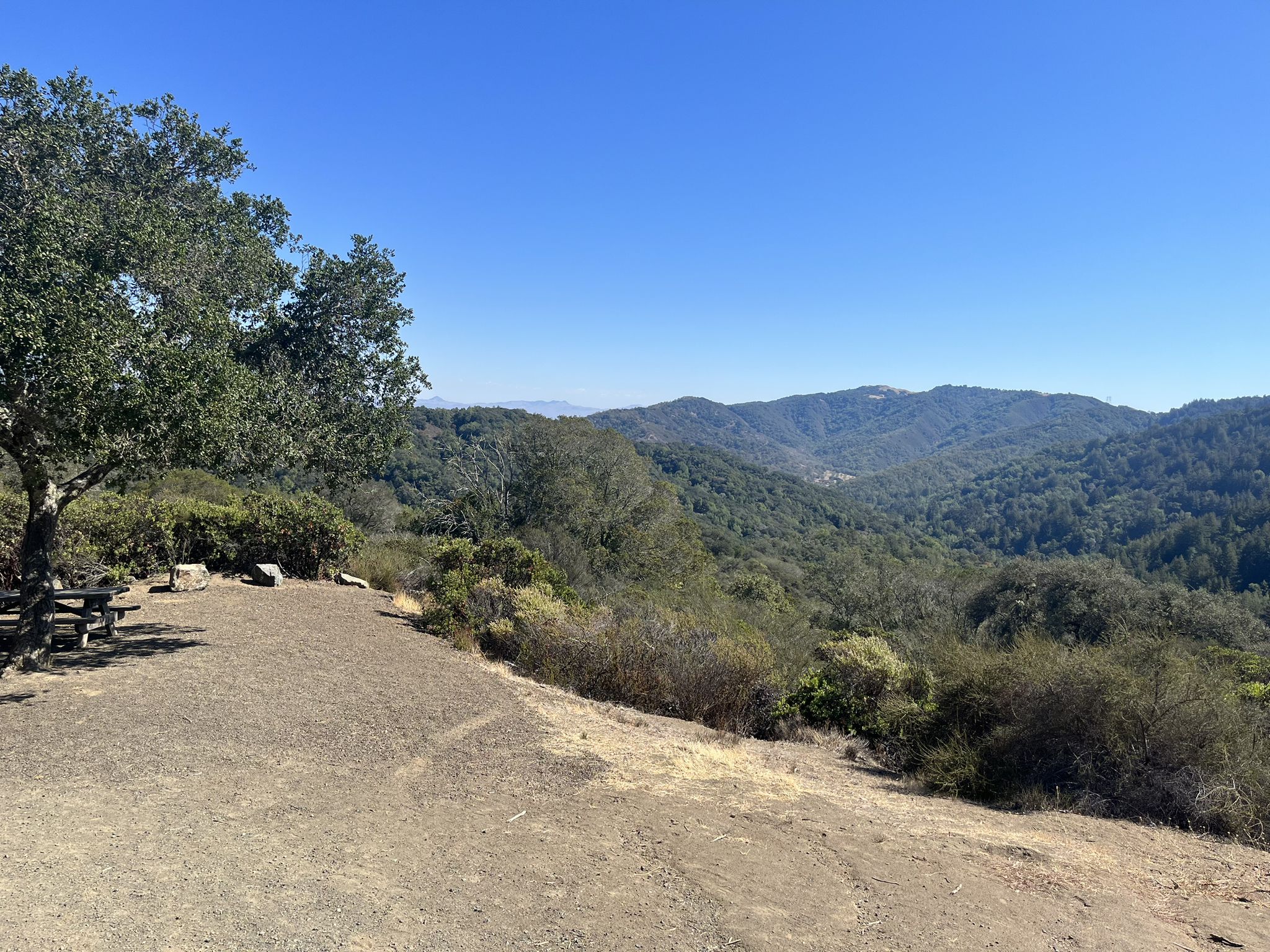 Sunny view of green rolling hills from a dirt clearing with a picnic table. - Nature Trail, Merry Go Round and Ridge Trail Loop