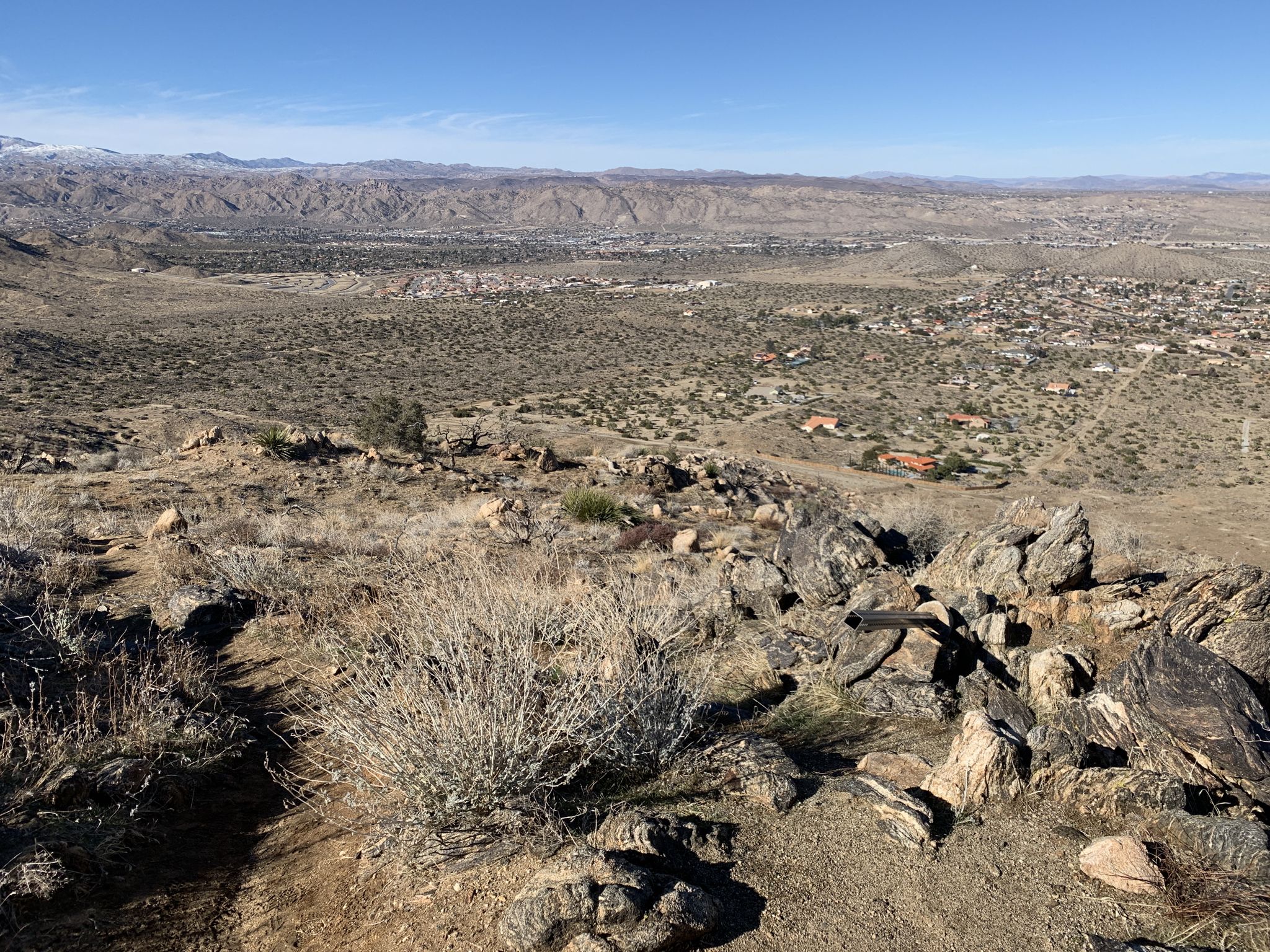 Vast desert landscape with rocky foreground, dry brush, and distant town. - South Park Peak Trail