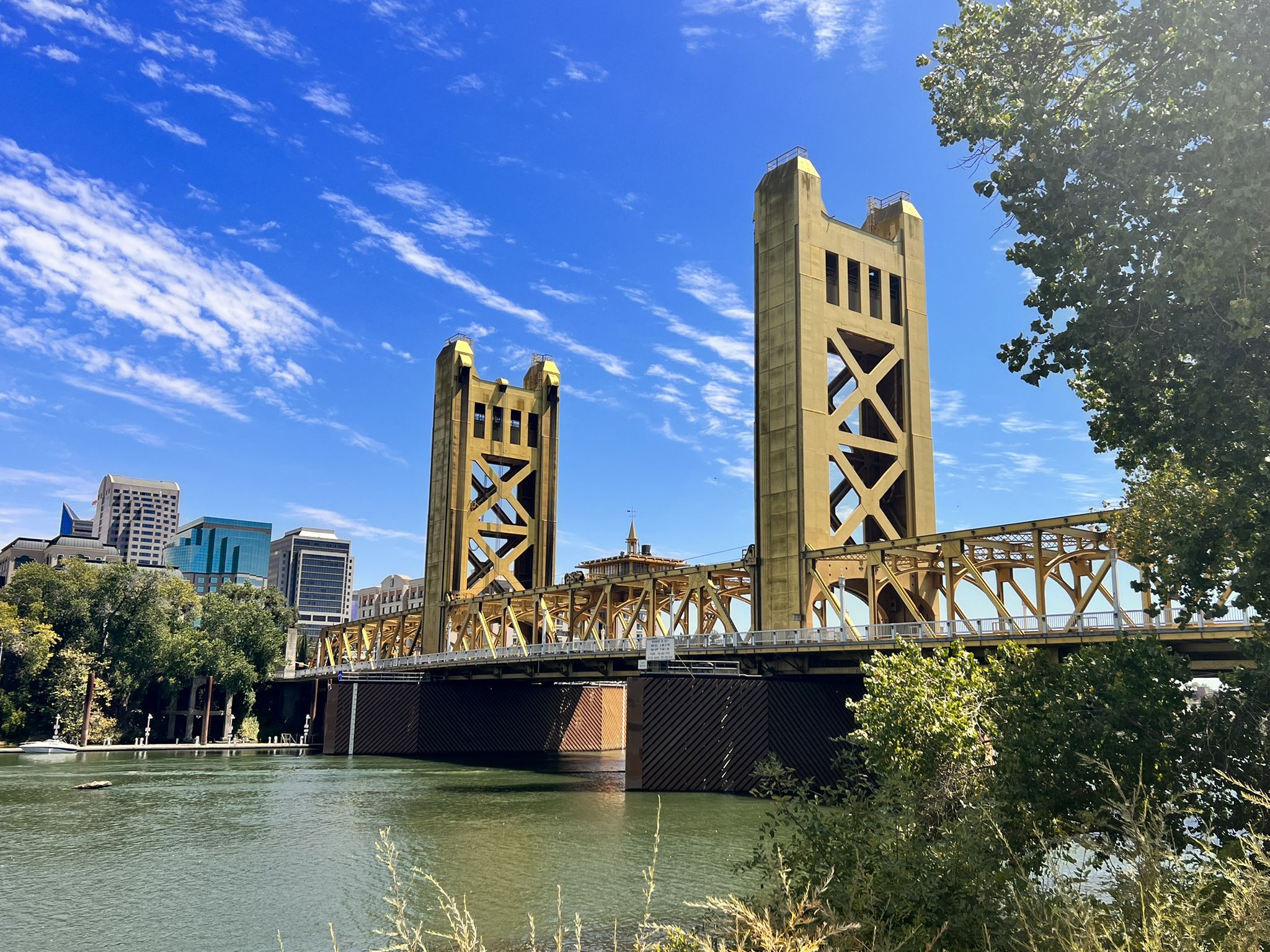 Golden bridge towers over a river with a city skyline under a blue sky. - River Walk Trail