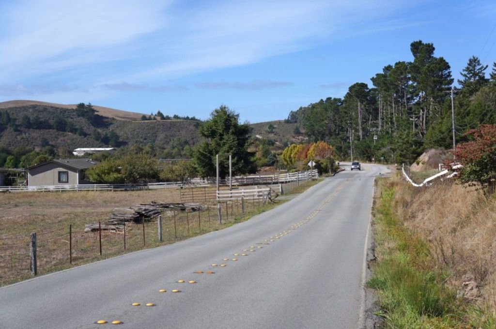 Paved road through a rural landscape with houses and hills under blue sky. - Downtown Pescadero loop from Loma Mar
