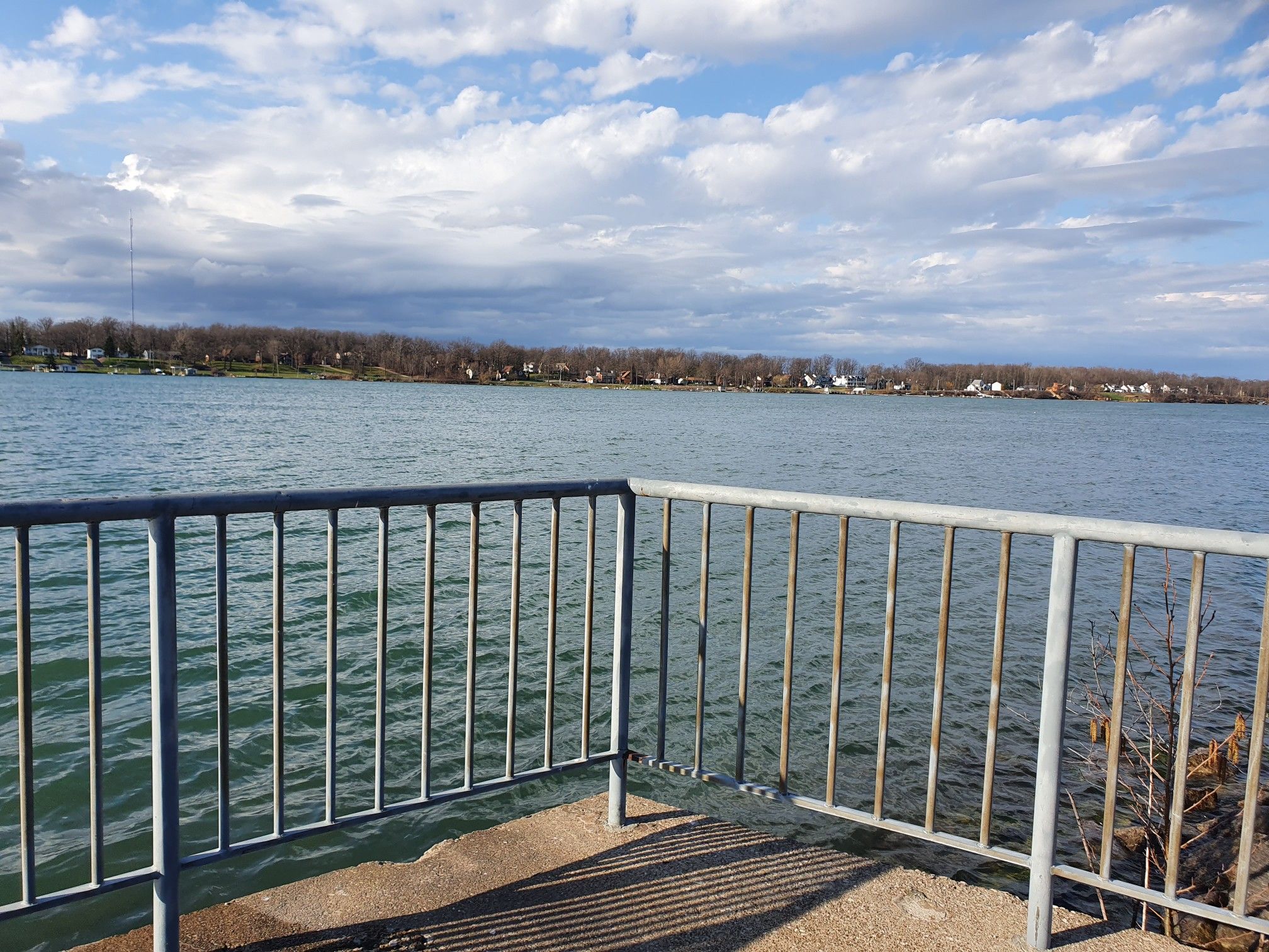 A metal railing overlooks a wide body of water with a distant treed shore. - Erie Canal Shoreline Trail from Scajaquada Creek to Veterans Park loop
