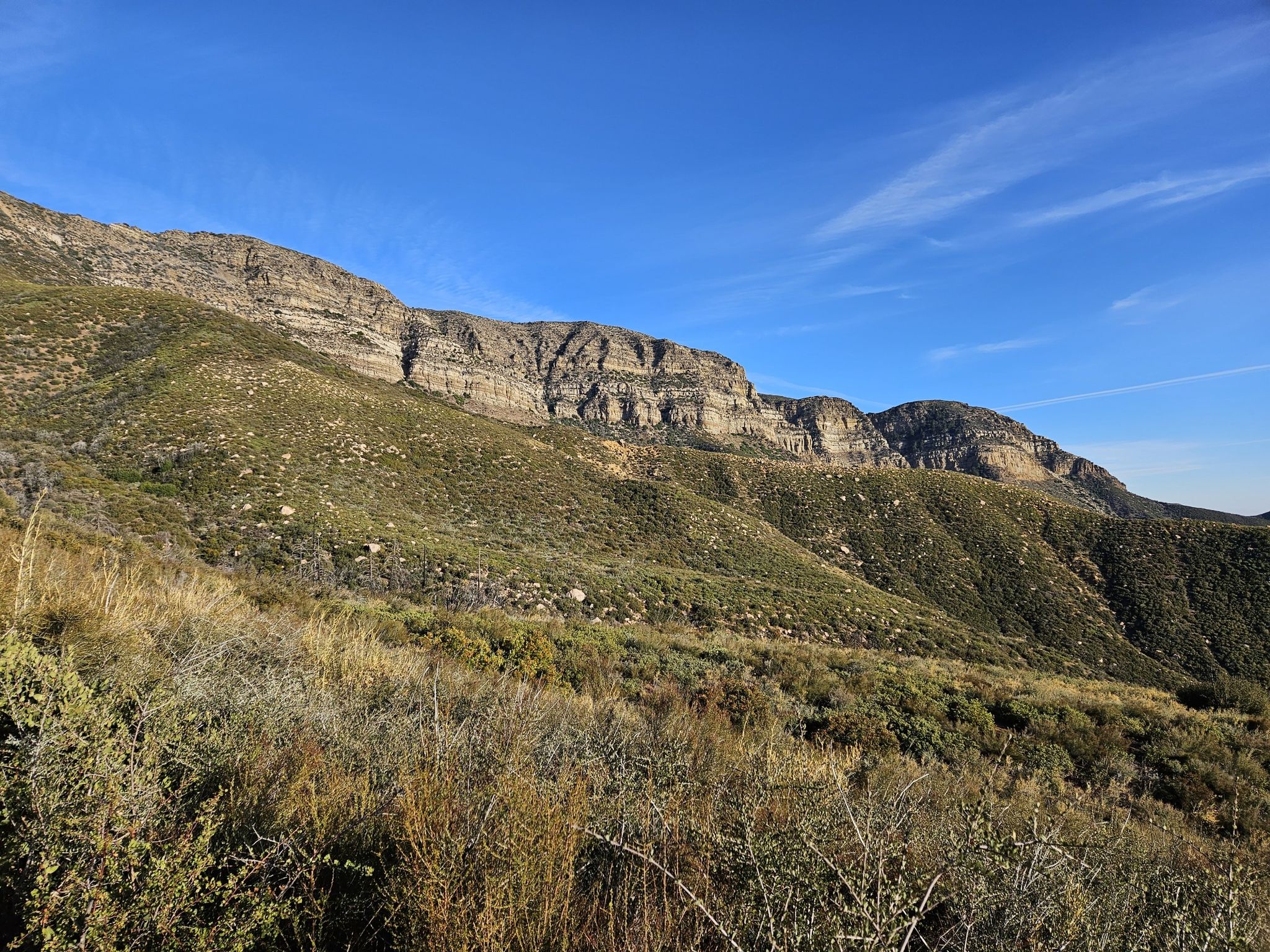 Majestic rocky mountain face covered in green scrub under a bright blue sky. - Topatopa Bluff Trail