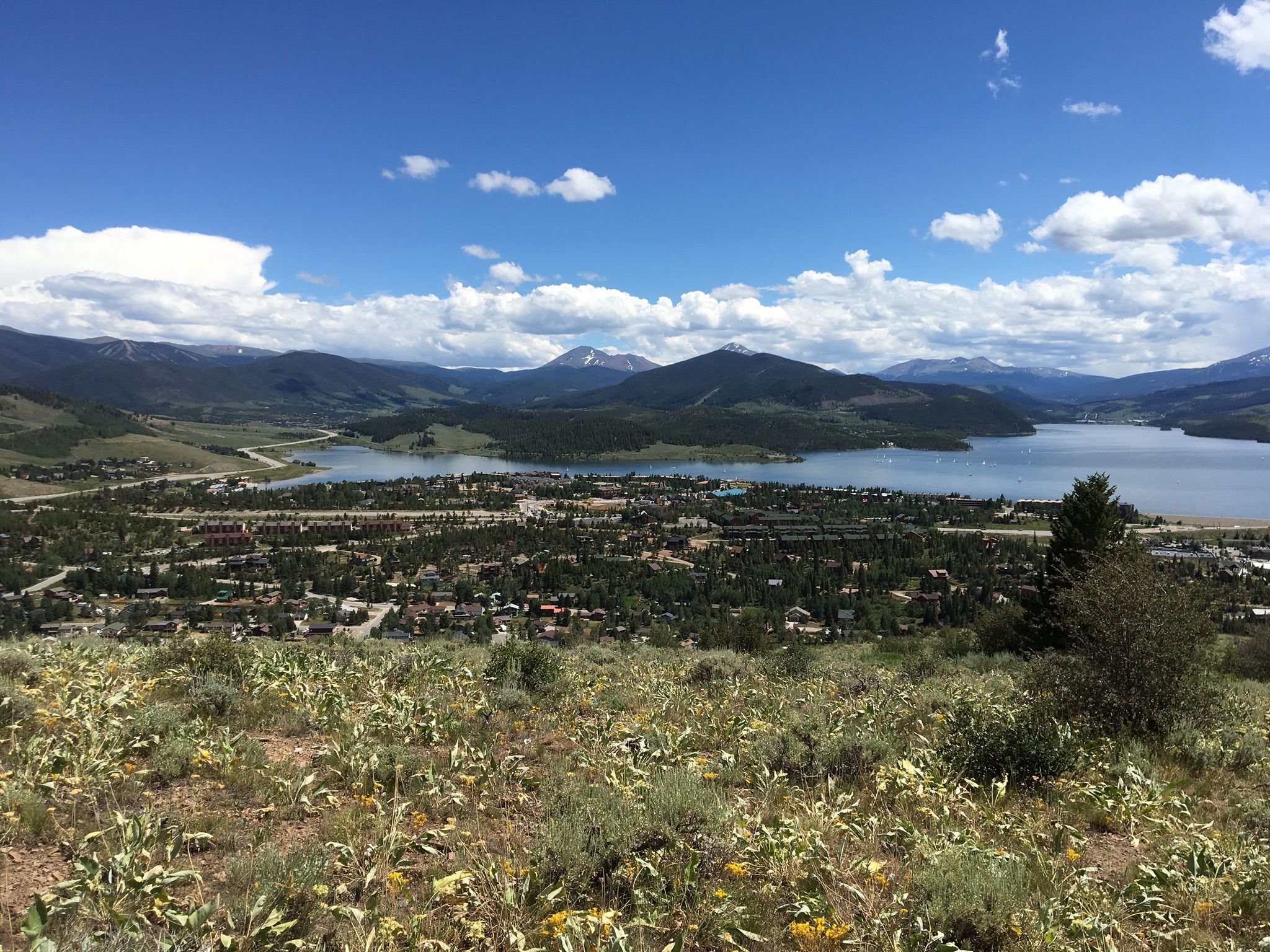 Panoramic view of a town and lake nestled in mountains under a blue sky. - Ptarmigan Loop Trail