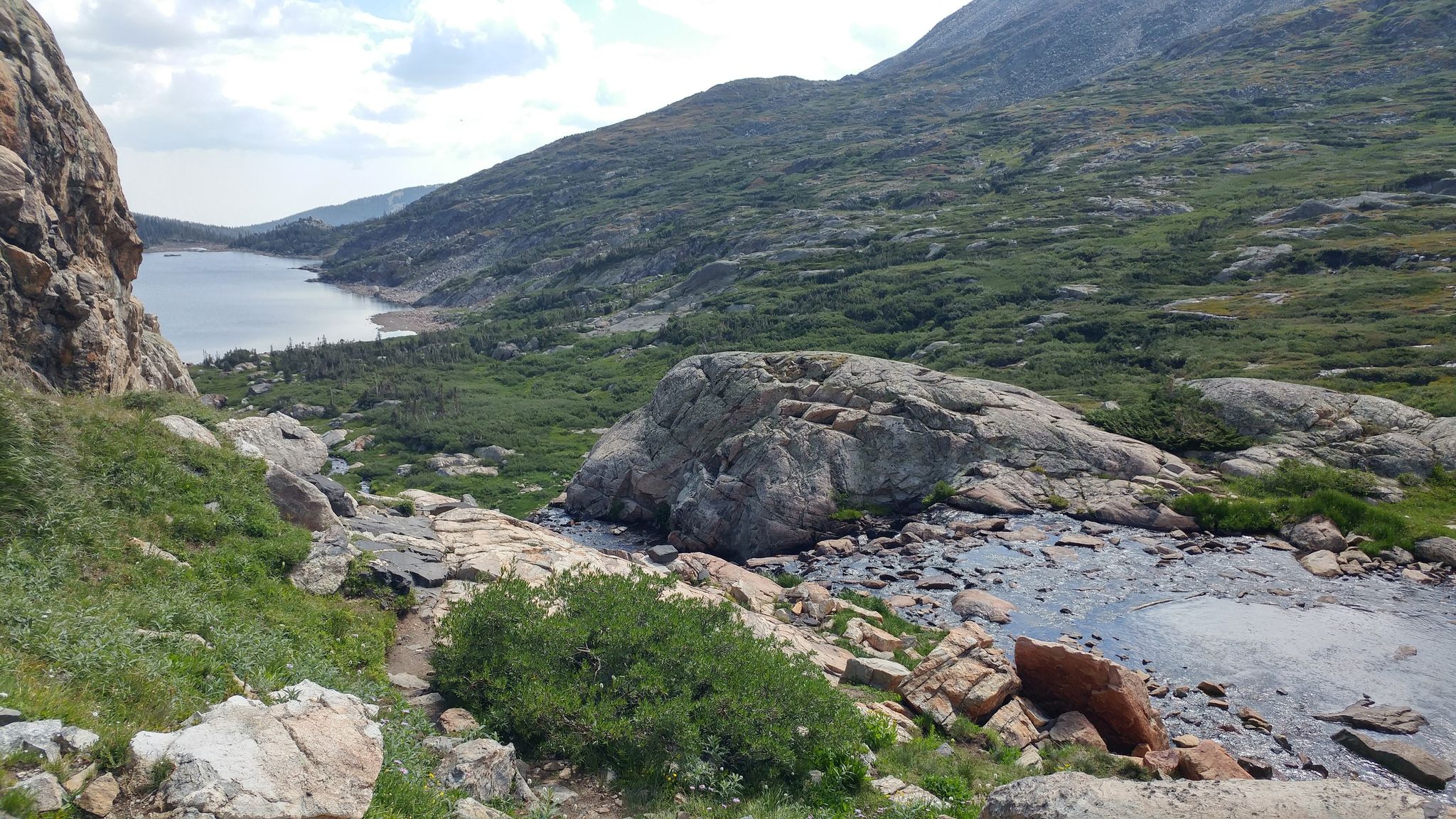 Mountain lake, rocky stream, and green hills under a cloudy sky. - Isabelle Glacier Trail