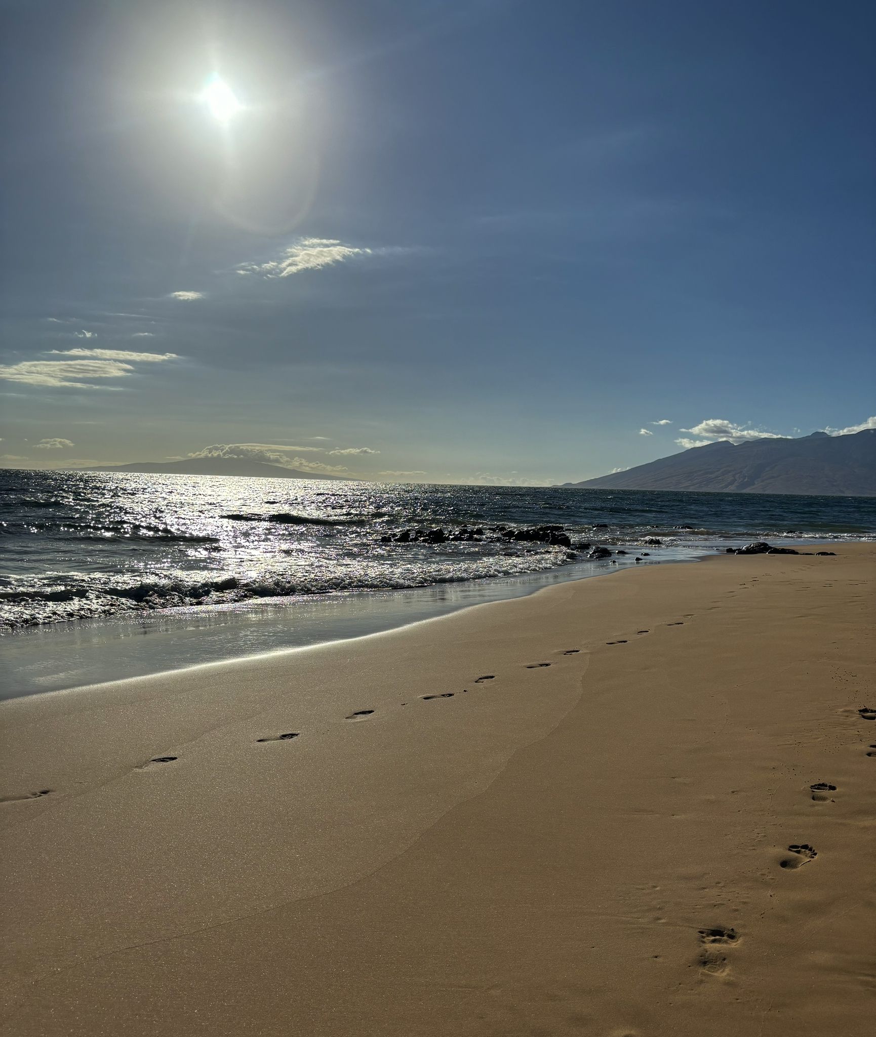 Bright sun over a sandy beach with footprints and sparkling ocean waves. - Ulua Beach Park to Keawakapu Beach