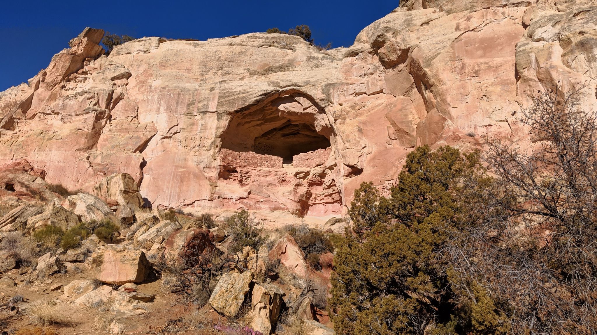 Large rock cliff with natural cave and ancient stone structure inside, blue sky. - Sand Canyon and East Rock Creek Loop