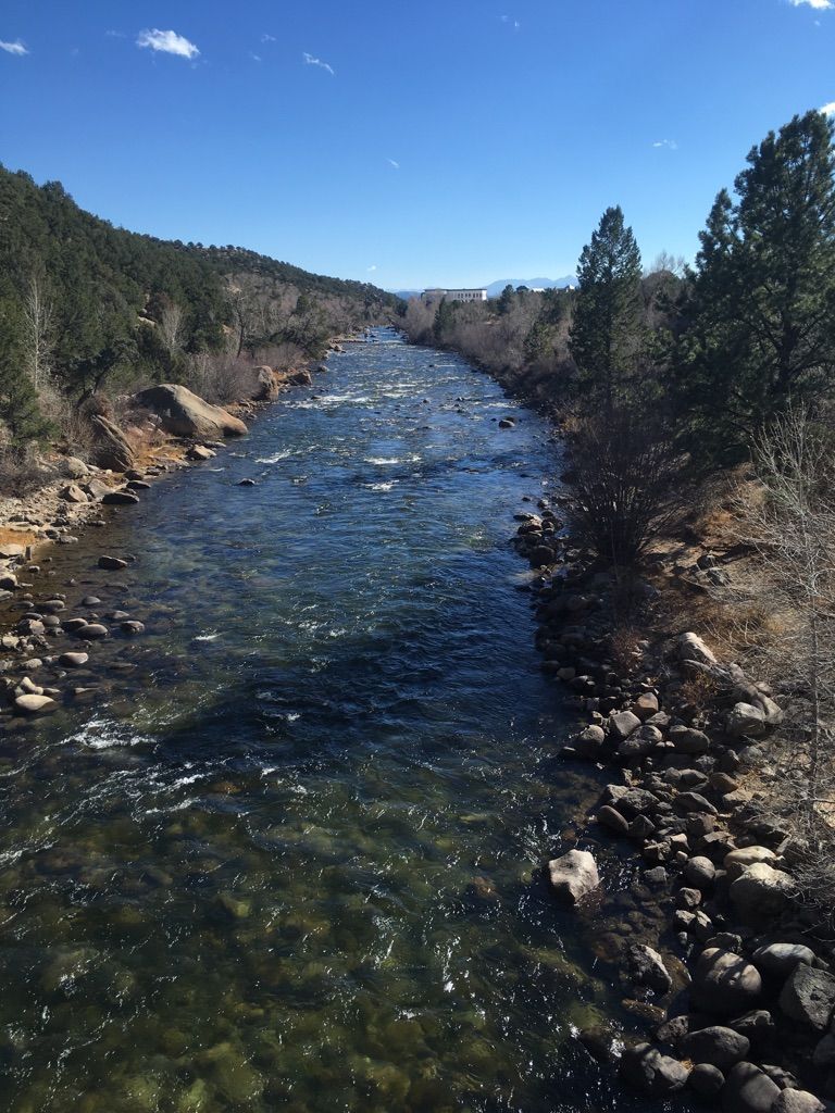 A clear, flowing river winds through rocky banks and green trees on a sunny day. - Midland Bike Trail & OHV Roads loop
